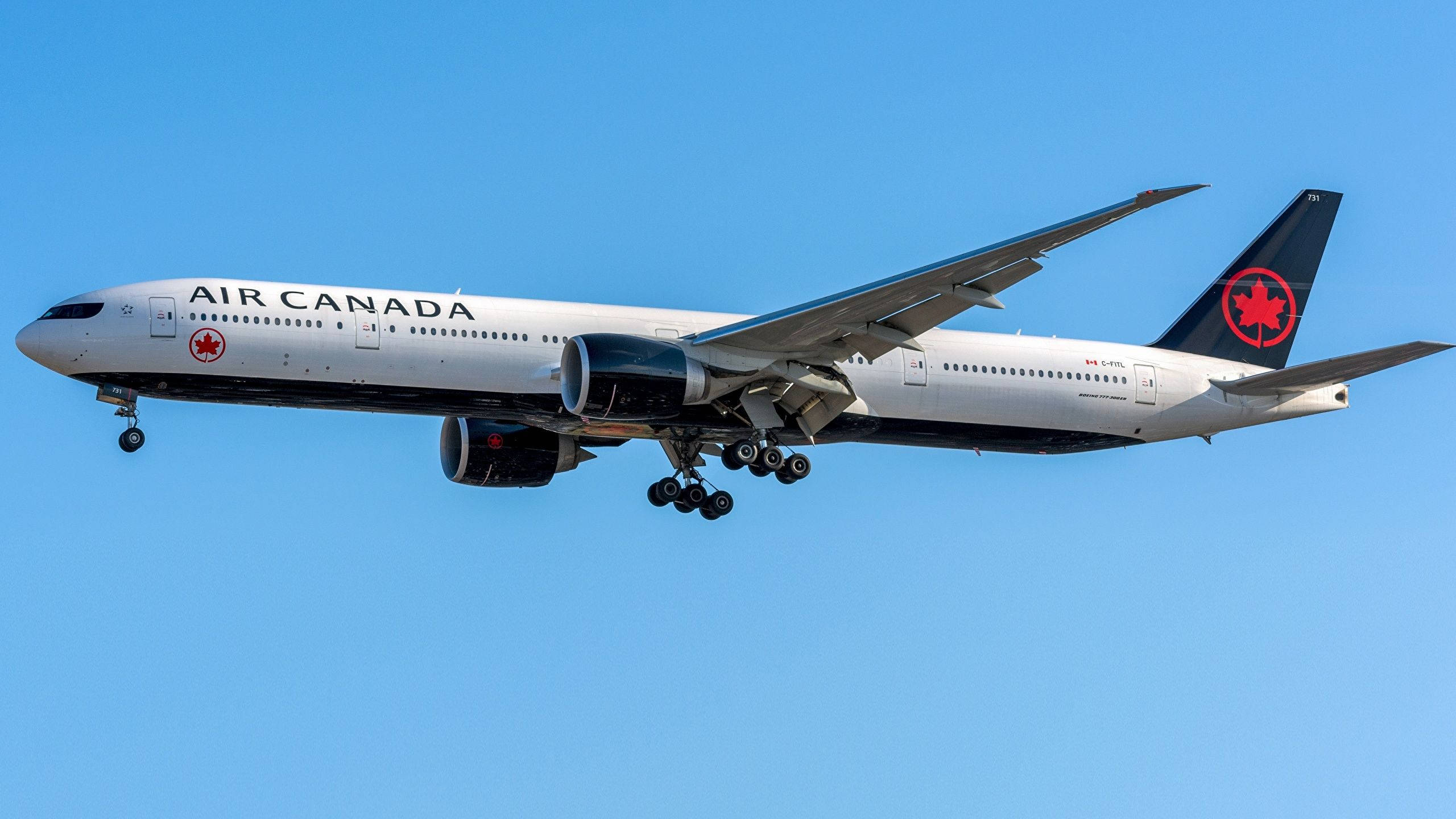 Air Canada飛機側面視圖 壁紙 — 一架加拿大航空波音777喺晴朗藍天下降落，起落架已放下。