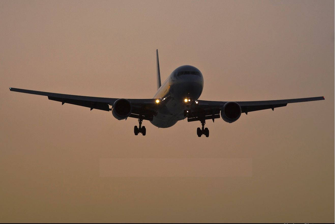 飛機在黃昏時降落，燈光在橙色天空中閃爍