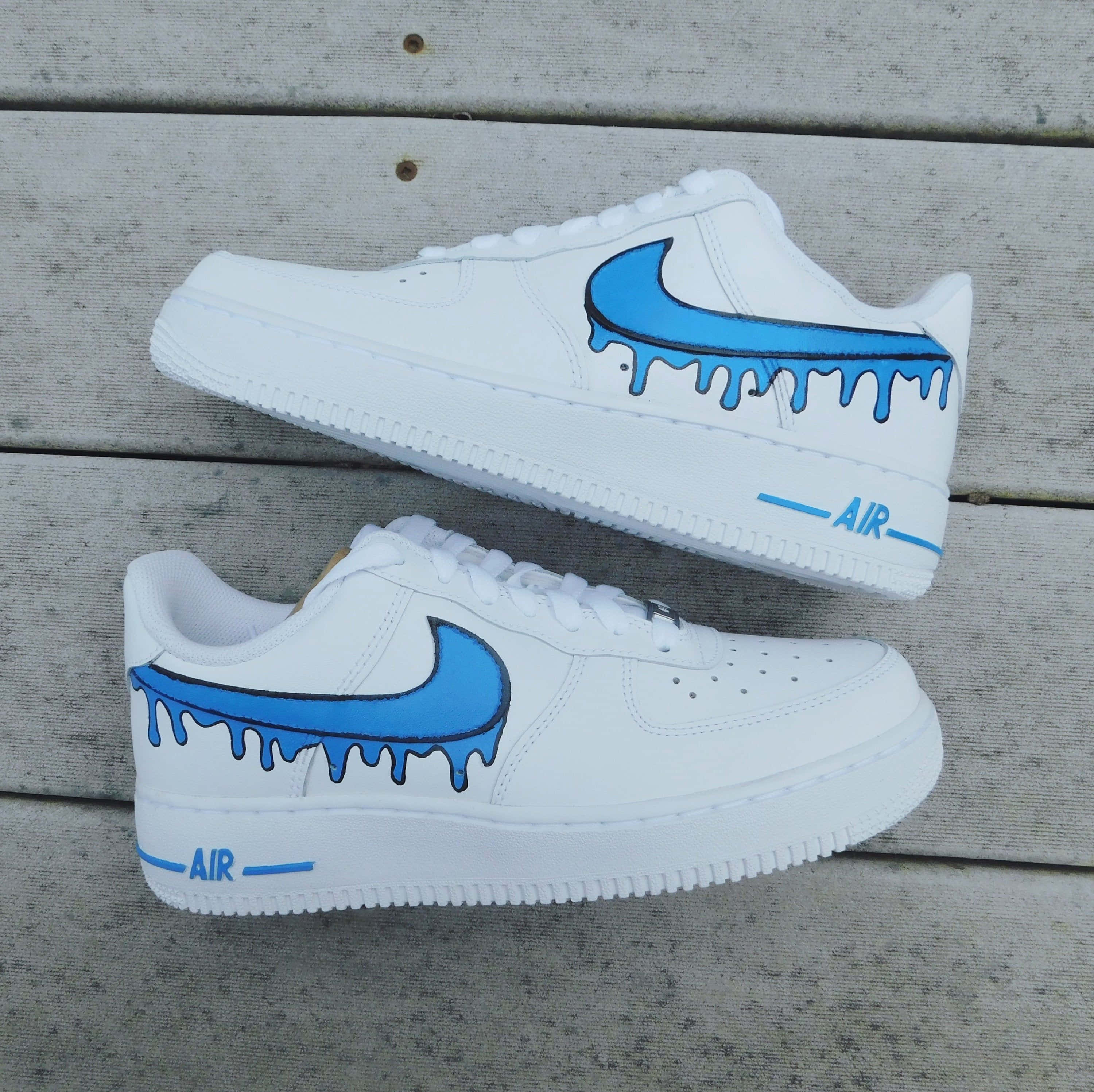 藍色滴染耐克 Air Force 1 壁紙 — 白色Nike Air Force 1運動鞋帶有藍色滴落Swoosh，放在風化的木板上。