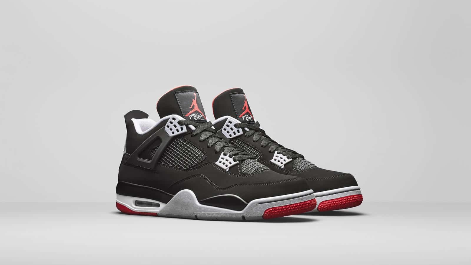 以 Air Jordan 4 探索飛躍時尚 壁紙 — 一對黑色Jordan 4運動鞋，帶有紅色點綴和白色鞋底，展示在極簡灰色背景上。