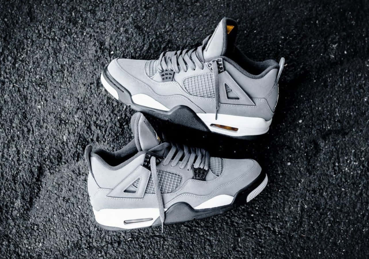灰色Jordan 4運動鞋搭配白色鞋底，位於深色瀝青表面。