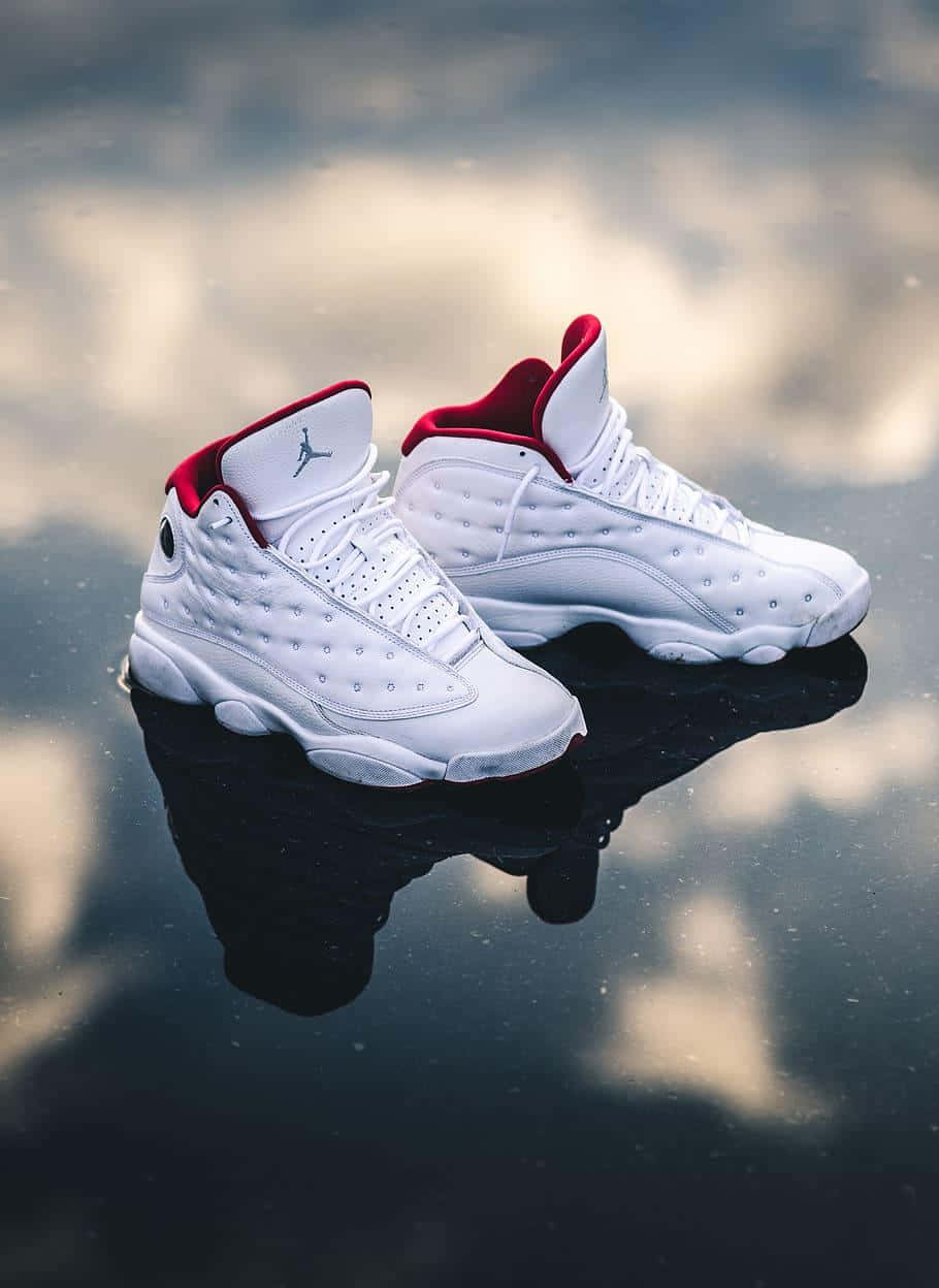 白色Jordan 13運動鞋帶有紅色點綴，置於反光的黑色表面上。