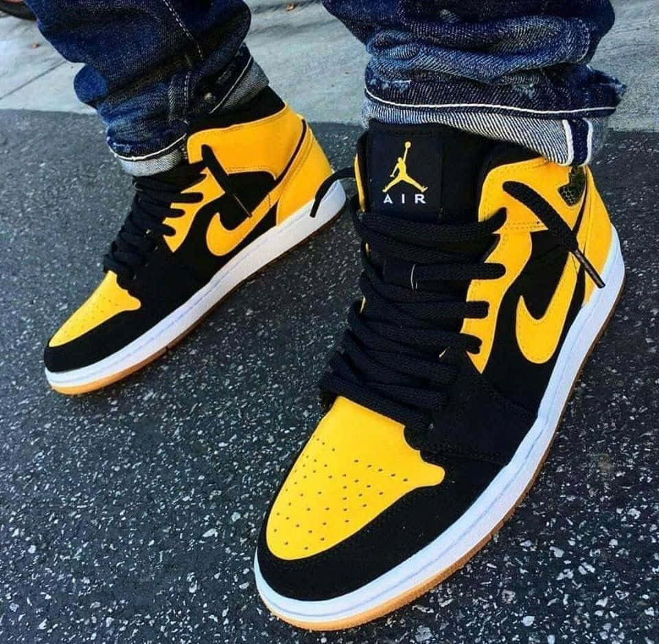 經典黃色Air Jordan球鞋 壁紙 — 黑色和黃色Jordan 1運動鞋特寫，搭配橡膠鞋底，穿著捲邊牛仔褲在瀝青路上。