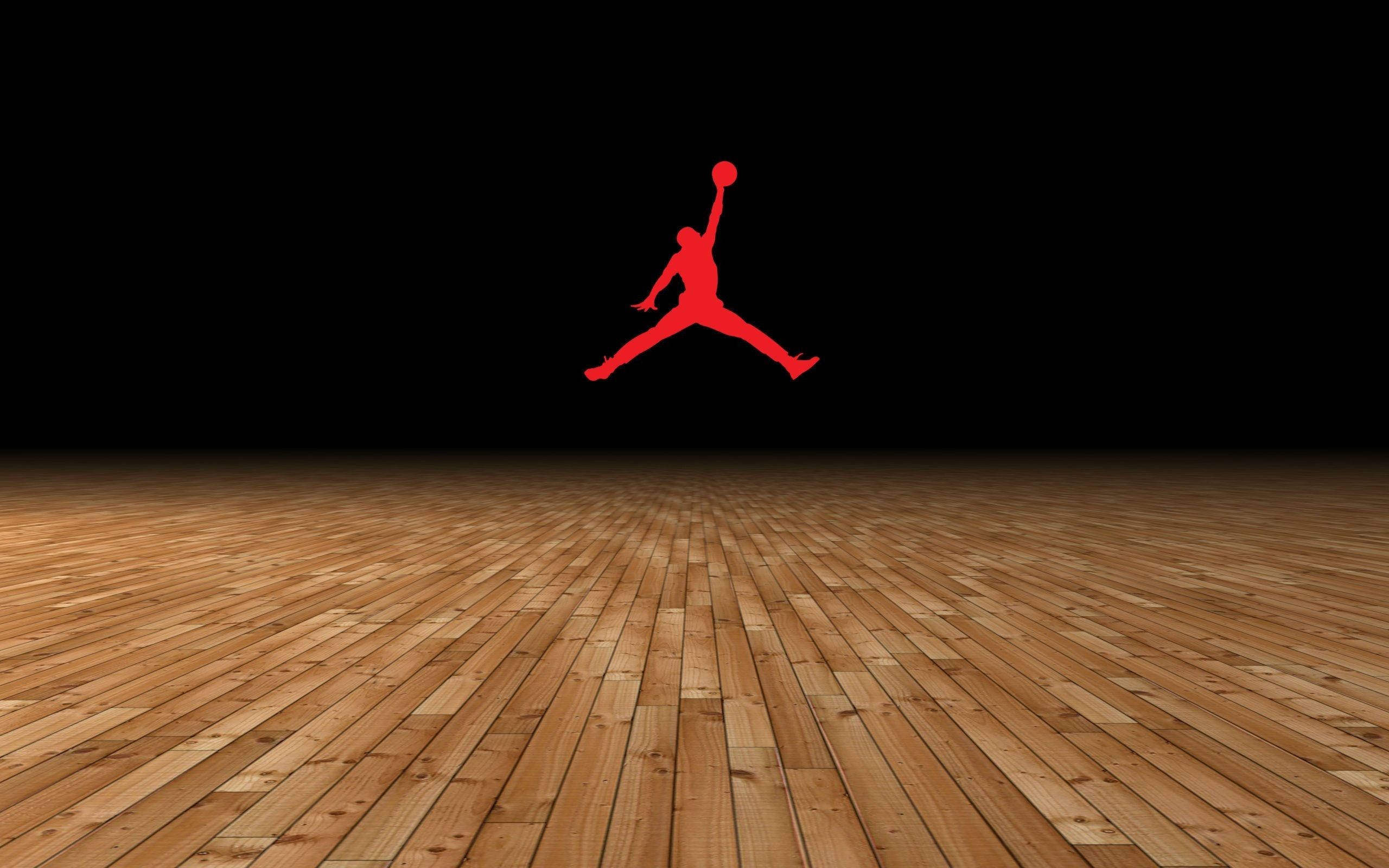 Air Jordan 木紋設計 壁紙 — 一個大膽的紅色Jordan標誌在黑色虛空下跳躍在拋光木製籃球場上方。