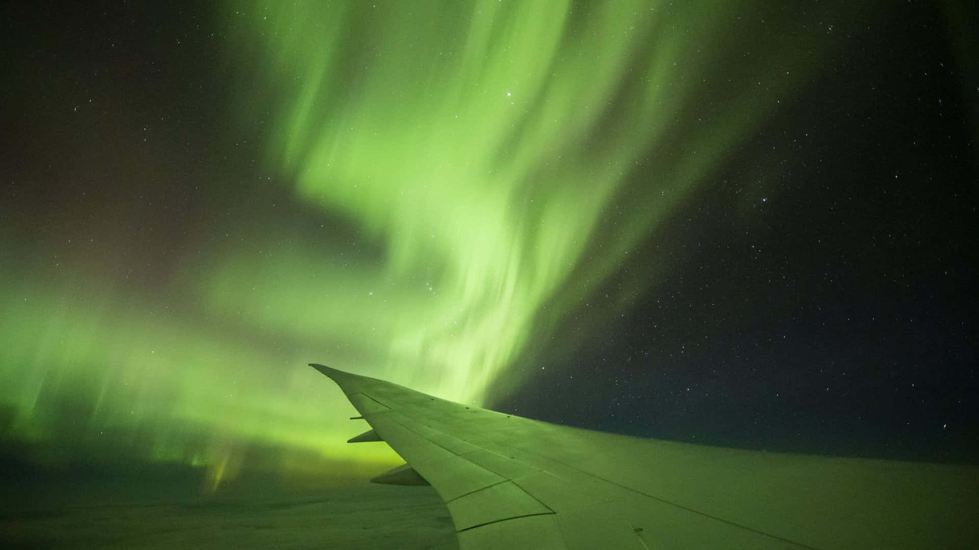  壁紙 — 飛機機翼剪影，背景係喺繁星夜空舞動嘅鮮綠色北極光。