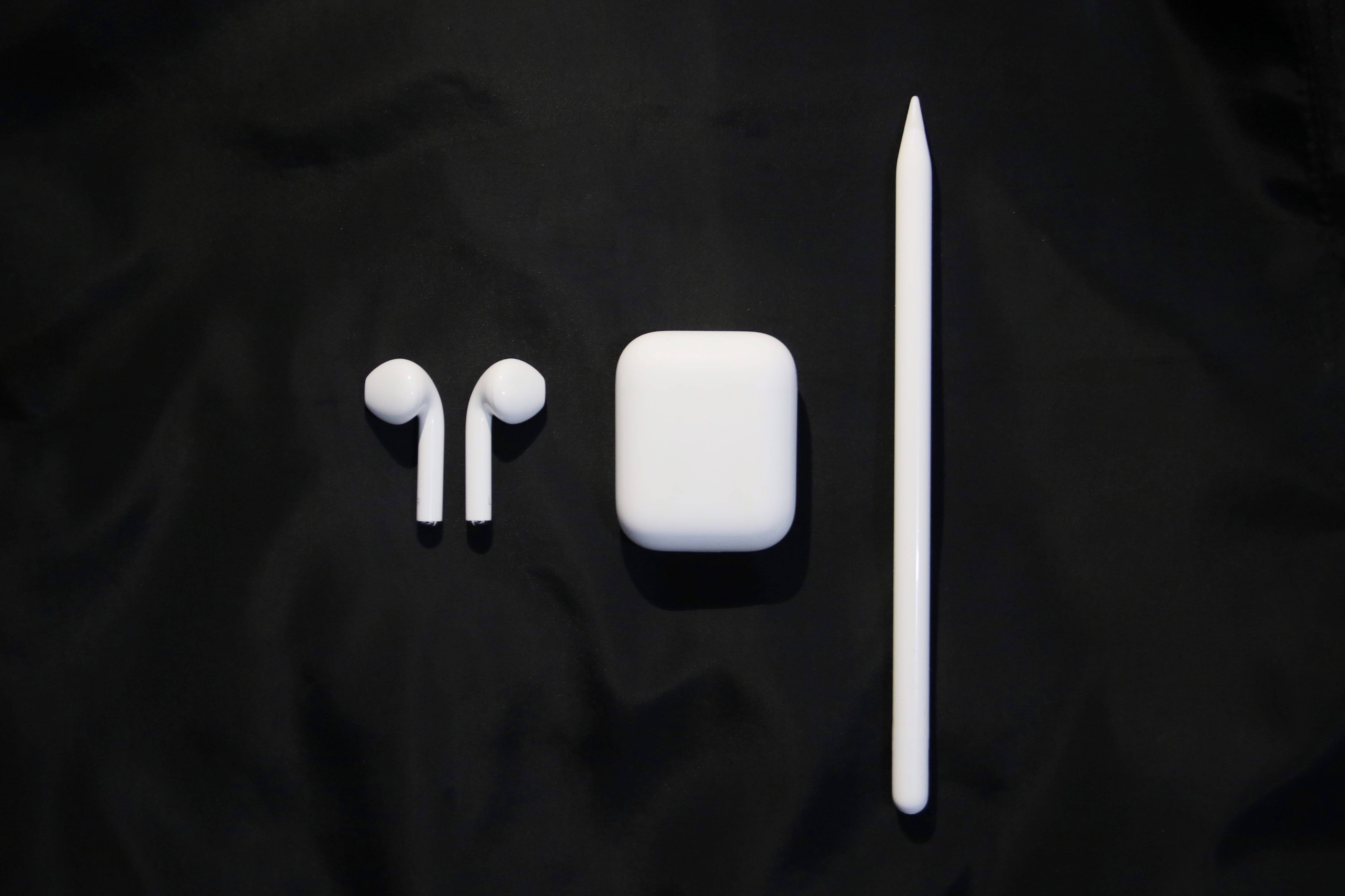 時尚白色 AirPods 與配件 壁紙 — 白色 Apple AirPods 保護殼、耳機和觸控筆整齊地排列在帶有紋理的黑色布料背景上。