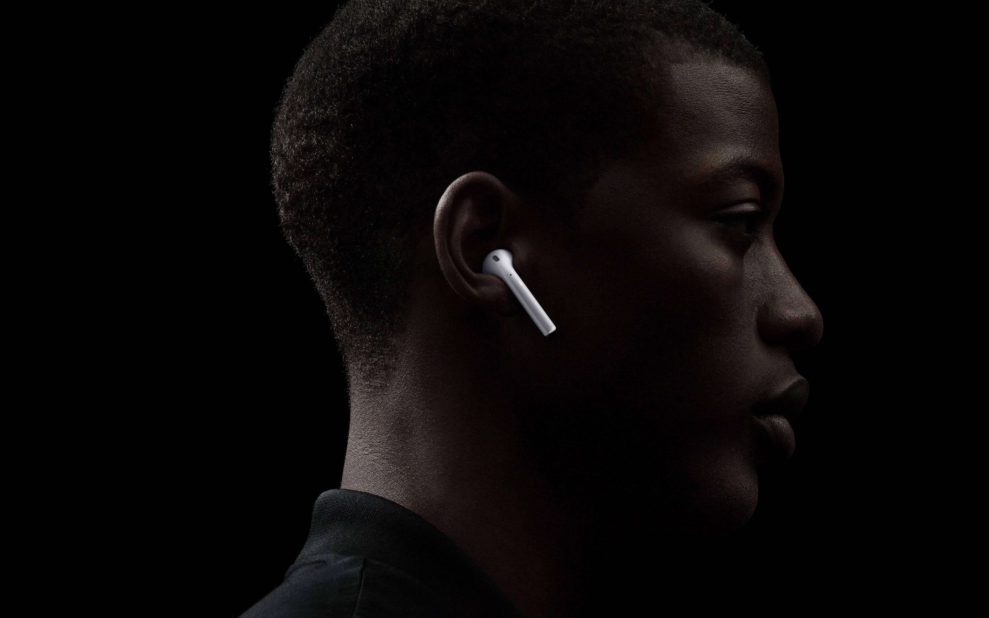 戴 AirPods 的男士 壁紙 — 一個人嘅側面，戴住白色無線耳機，背景係純黑色，燈光效果強烈。
