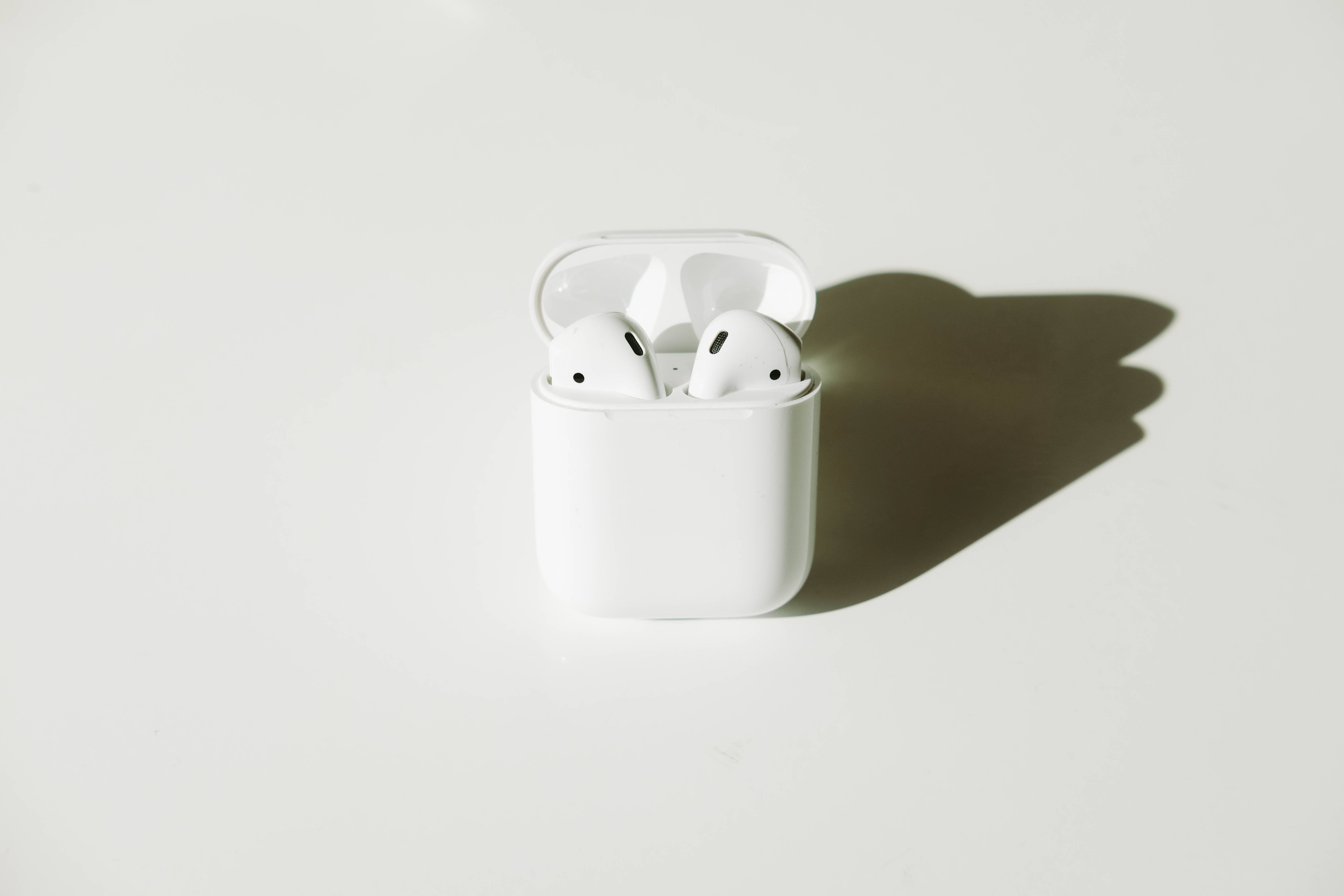 第二代白色 AirPods 壁紙 — 白色無線耳機整齊地放在打開的充電盒中，在極簡白色表面上投下清晰的陰影。