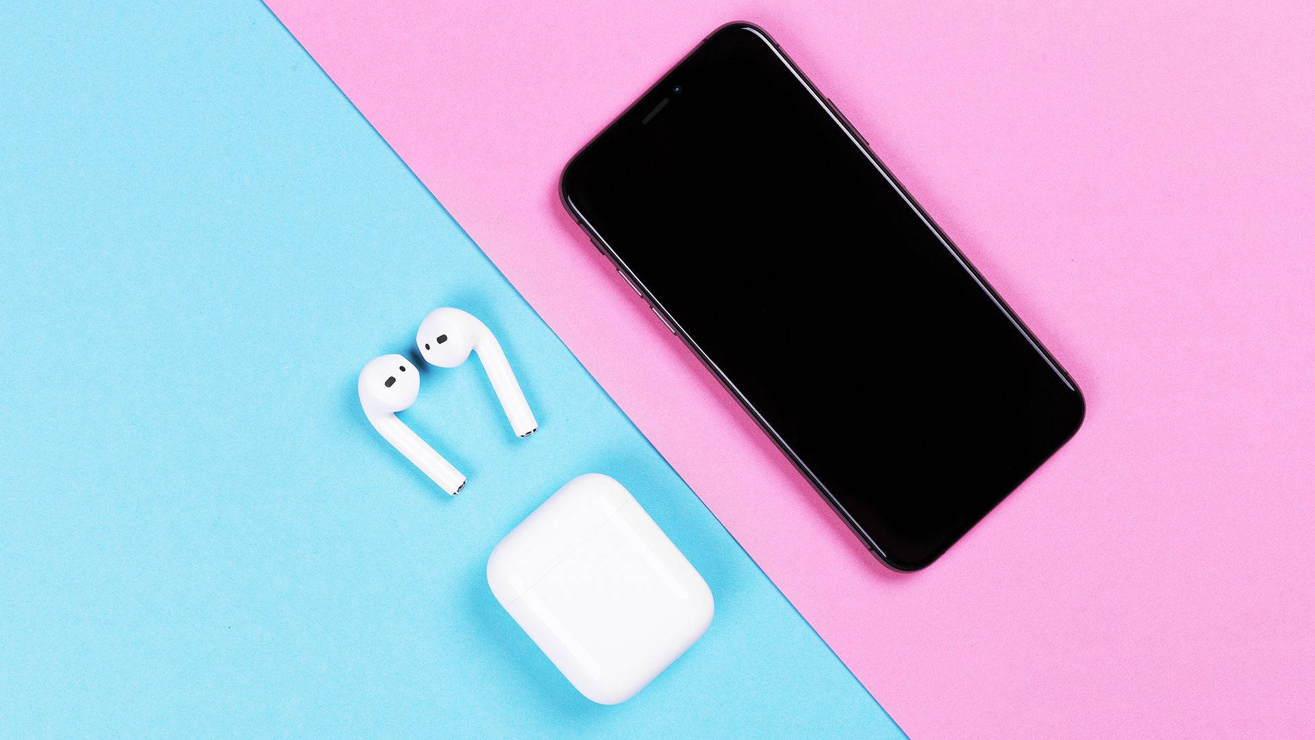 粉藍 AirPods 壁紙 — 白色無線耳機和充電盒放在黑色智能手機旁邊，背景為粉紅色和藍色分割。