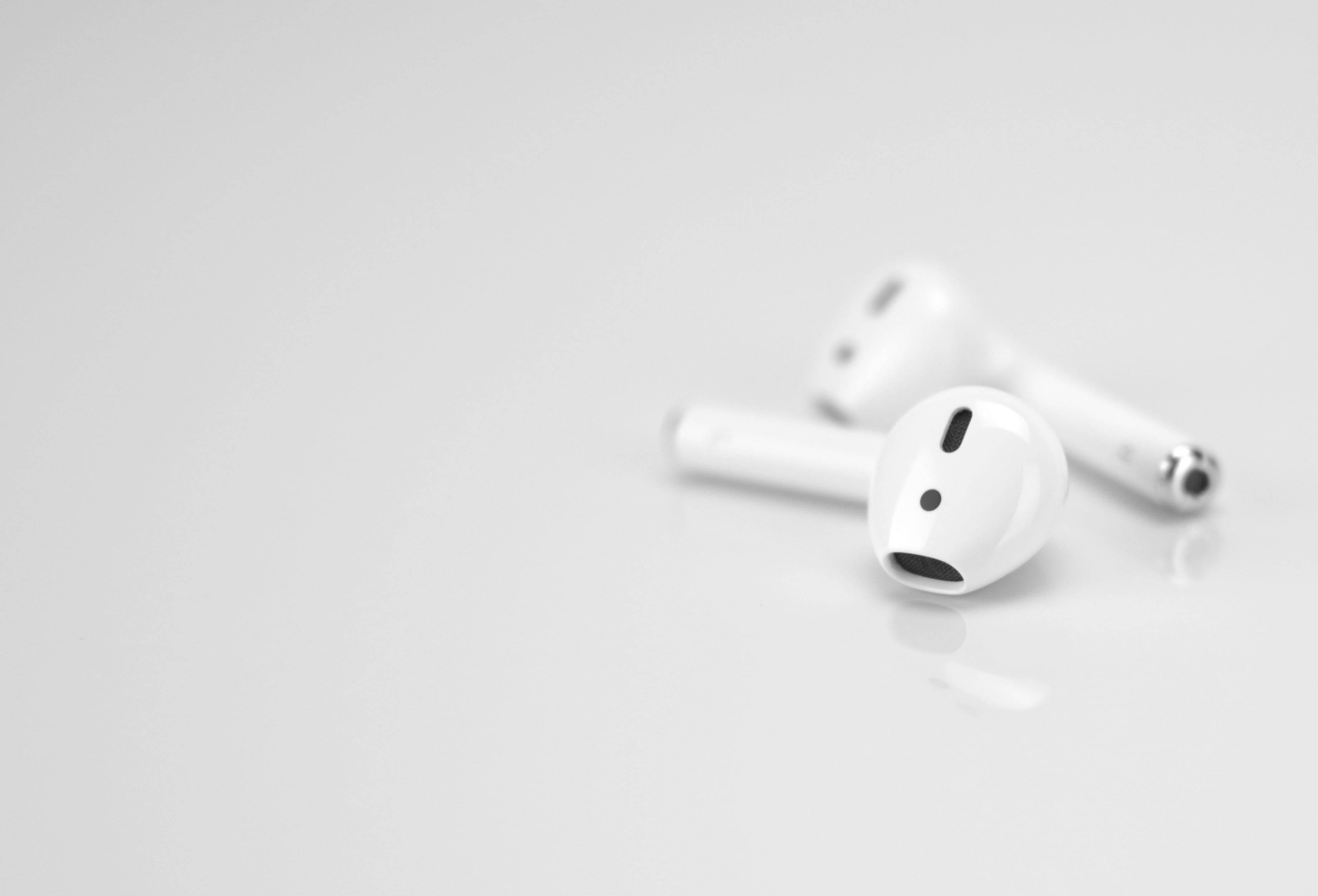 簡約第二代 AirPods 壁紙 — 兩個白色無線耳塞放在一個極簡風格的反射表面上，帶有柔和陰影和淺景深。
