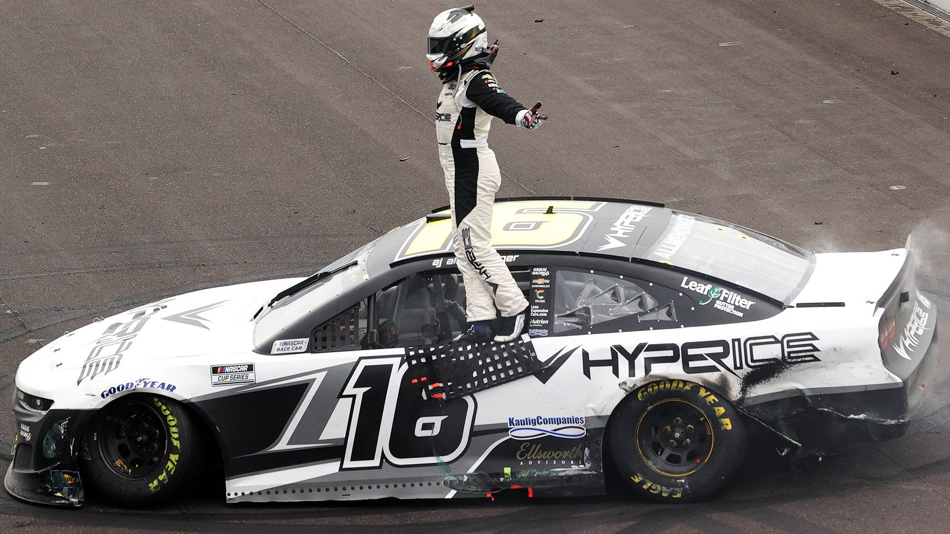 AJ Allmendinger 站在車窗上 壁紙 — 一名身穿全套裝備的賽車手勝利地站在他受損的#16 NASCAR賽車車頂上，賽道上後輪胎冒出滾滾濃煙。