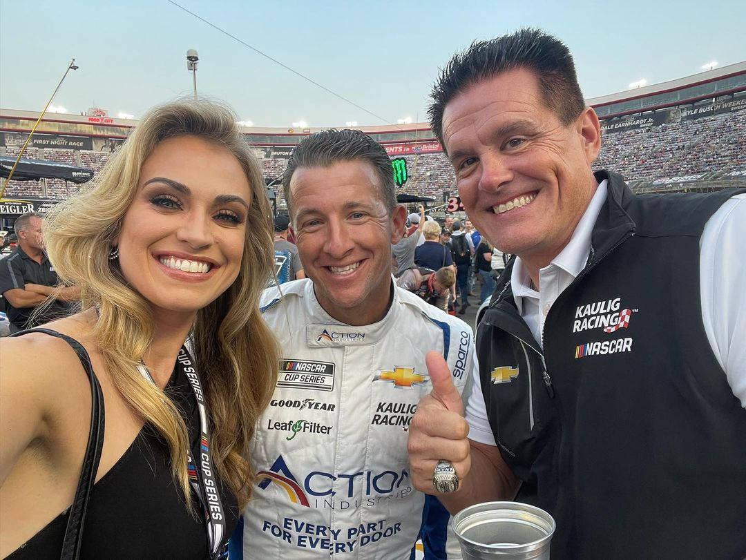 三位微笑的NASCAR人士在賽道上擺姿勢自拍。