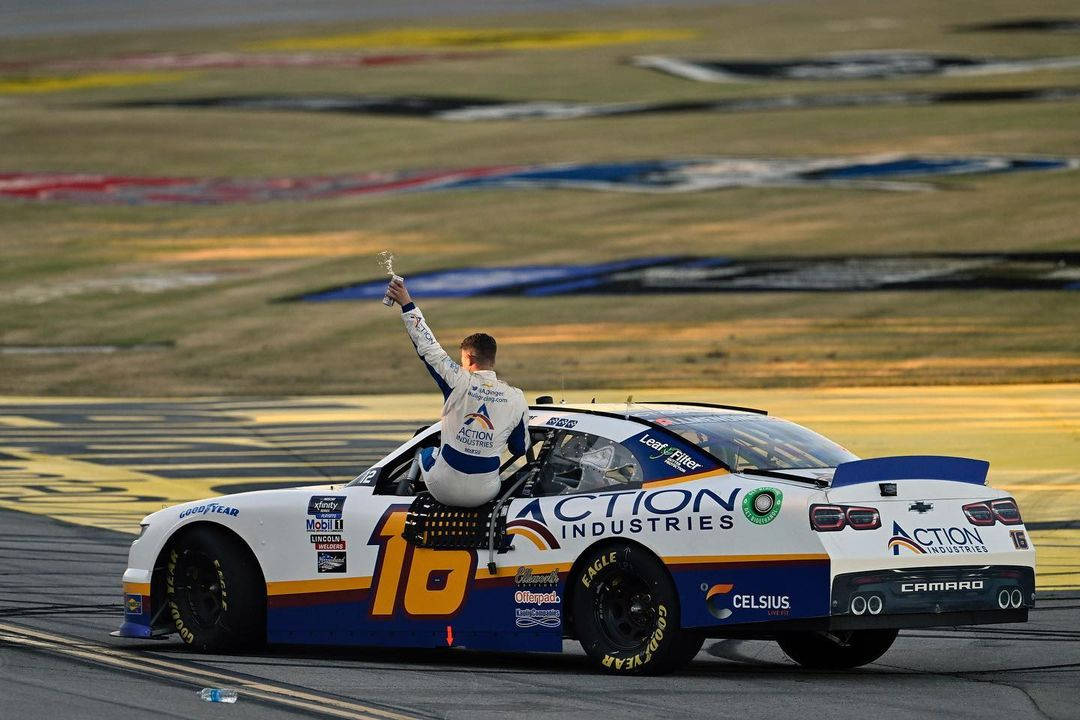 NASCAR車手在日落時分在賽車上舉起獎盃慶祝勝利。