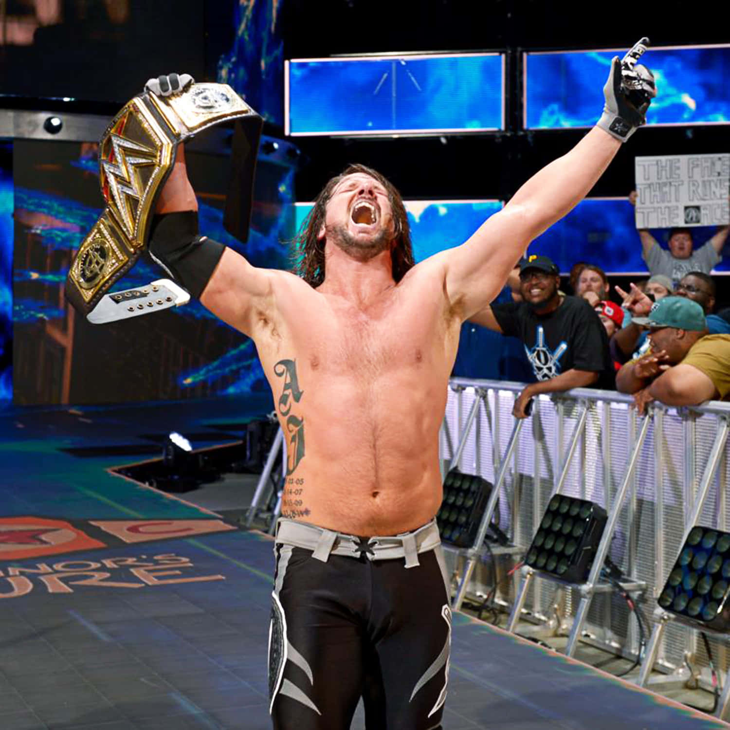 AJ Styles WWE Raw冠軍 壁紙 — 摔角手在燈光明亮的擂台上，勝利地高舉冠軍腰帶和拳頭，發出震耳欲聾的勝利呼喊。