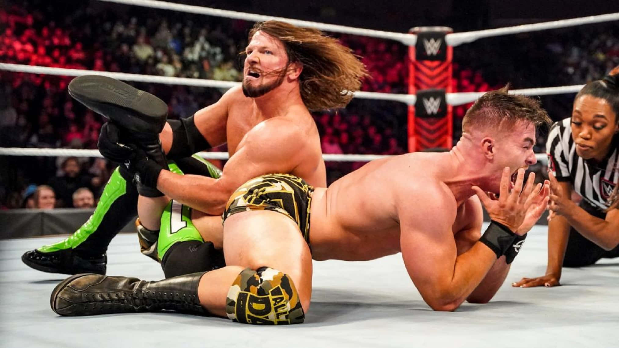 AJ Styles 對 Austin Theory 降服 壁紙 — 穿著黑色靴子的摔角手在擂台上對對手使出高衝擊力招式，裁判在旁仔細觀察。