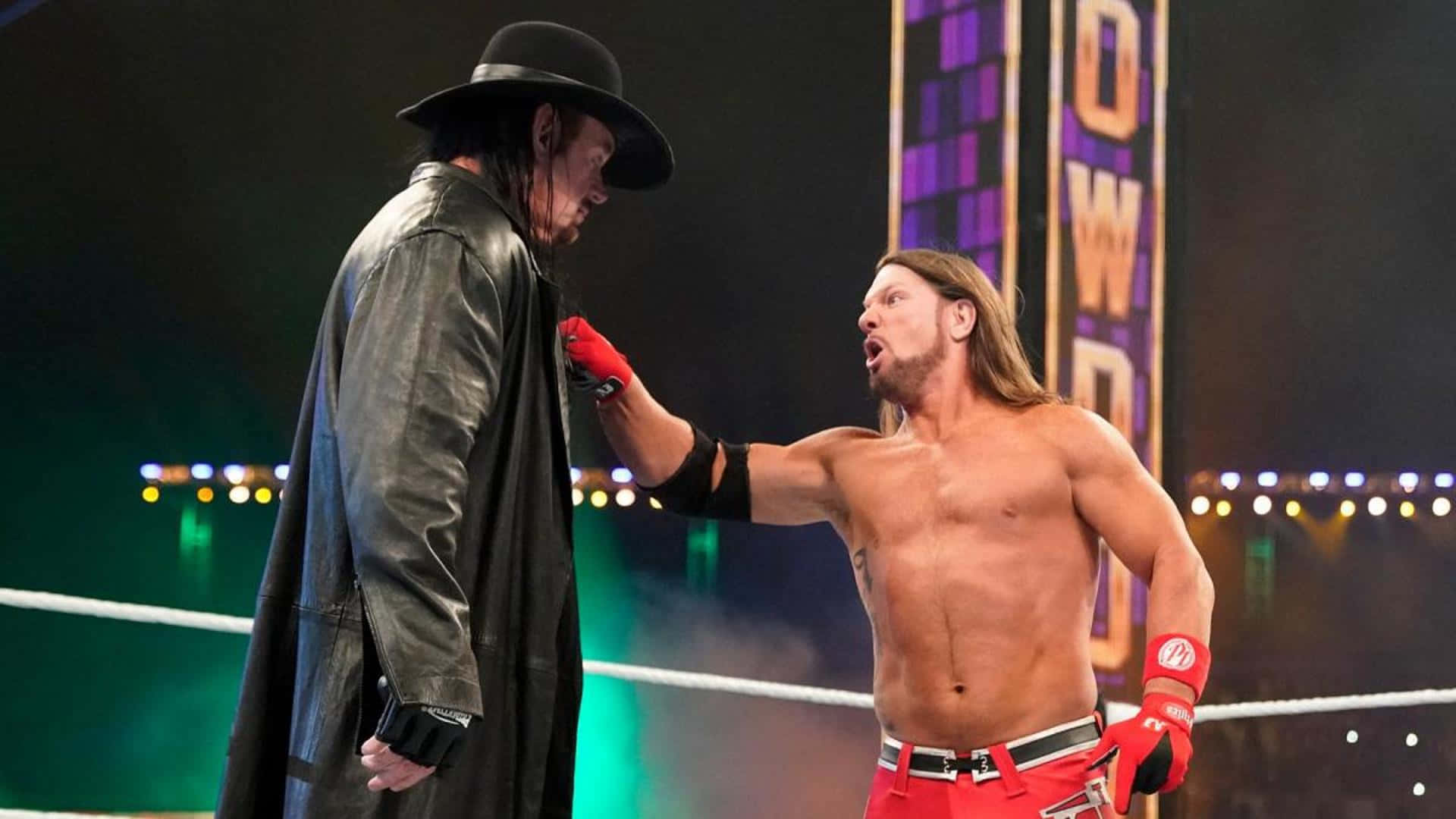 AJ Styles 挑戰 The Undertaker 壁紙 — 兩名WWE摔角手在擂台上對峙，一人身穿黑色風衣和帽子，另一人赤裸上身，戴紅色手套和穿紅色褲子。