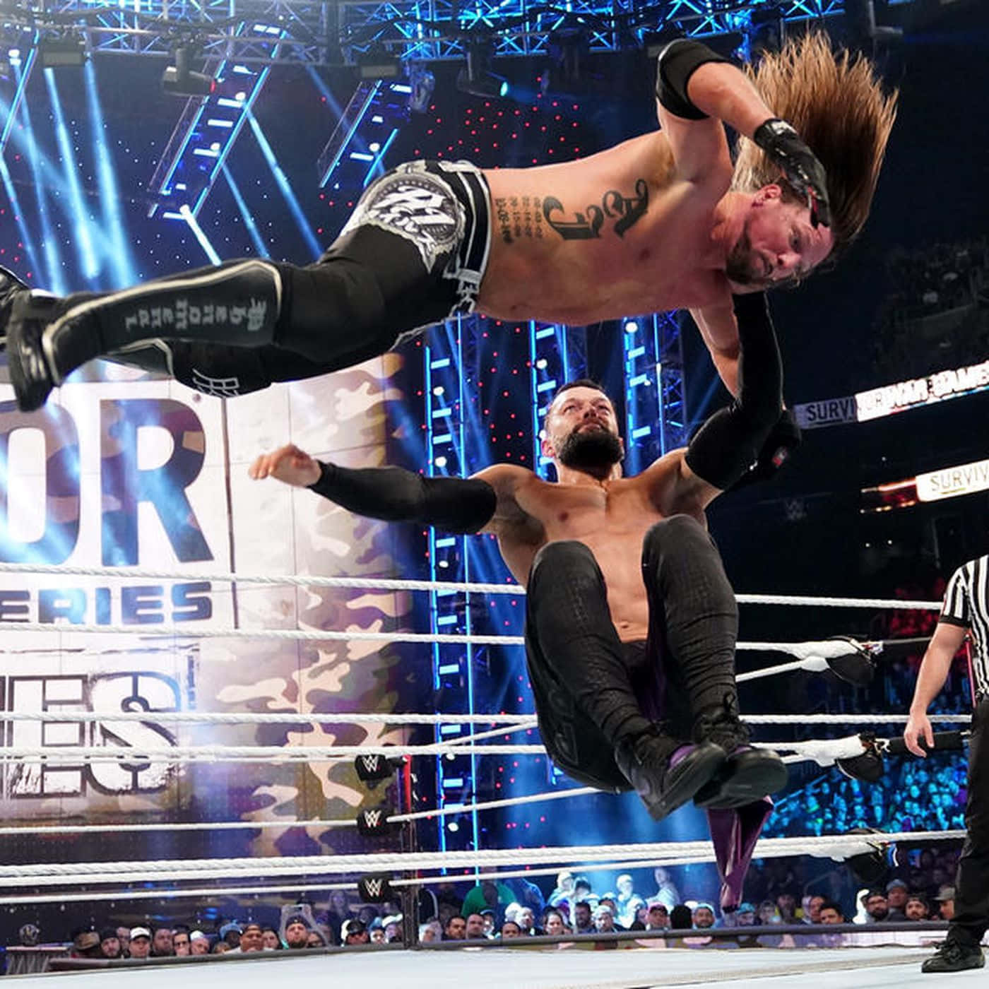 AJ Styles 破織天際 壁紙 — 一名摔角手在半空中躍起，在燈光明亮的摔角場內對對手施展高空飛行動作。