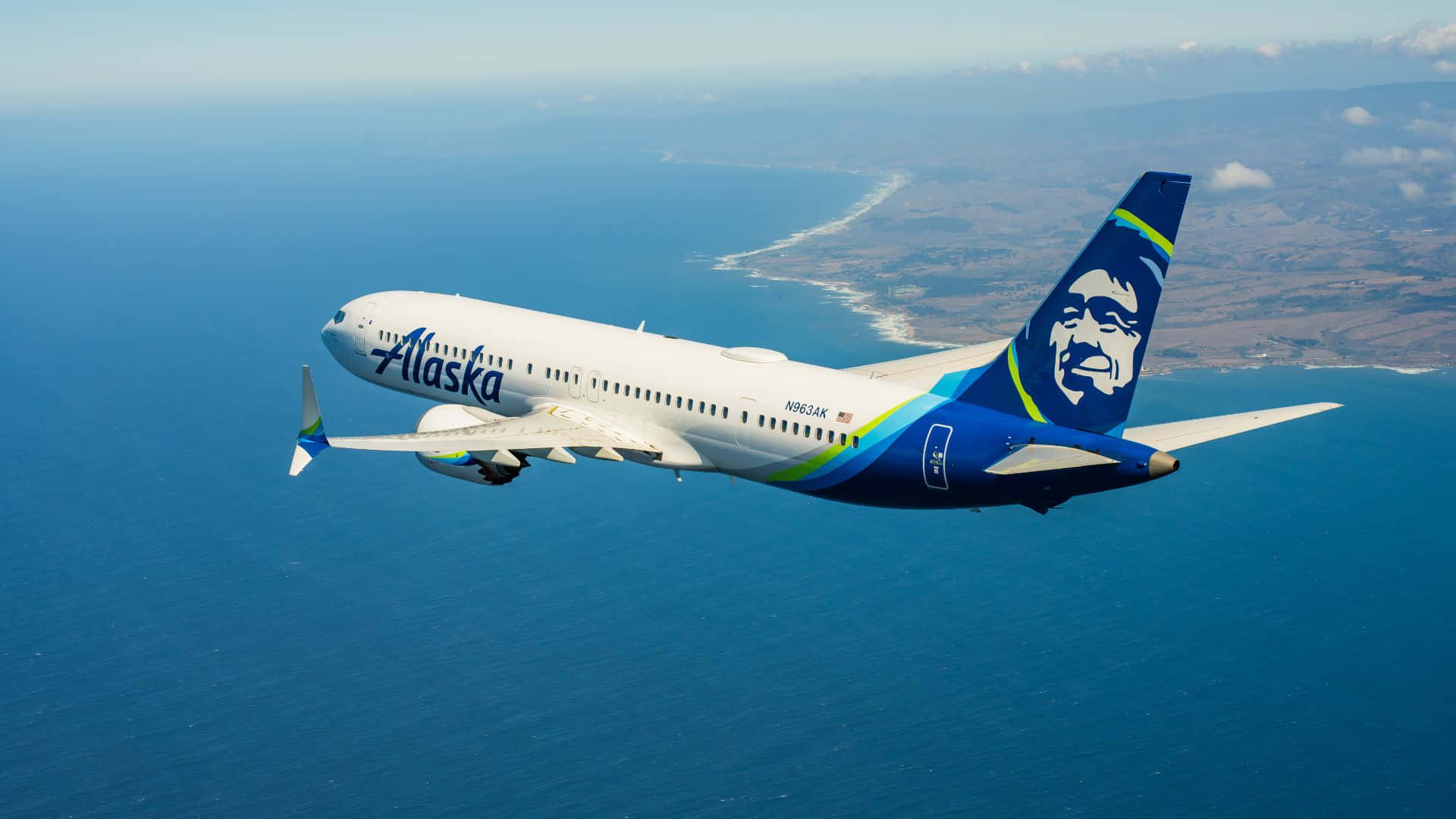  壁紙 — 阿拉斯加航空的飛機在廣闊的藍色海洋上空翱翔，下方可見沿海陸地。