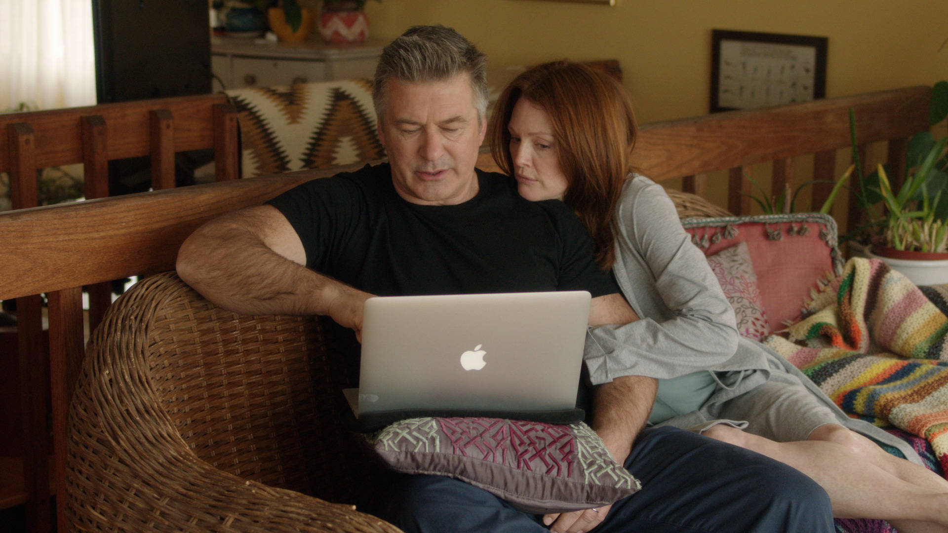 Alec Baldwin 與 Julianne Moore 壁紙 — 一對情侶在室內共享寧靜時刻，一起專注於筆記型電腦，身處舒適、燈光溫暖的客廳。