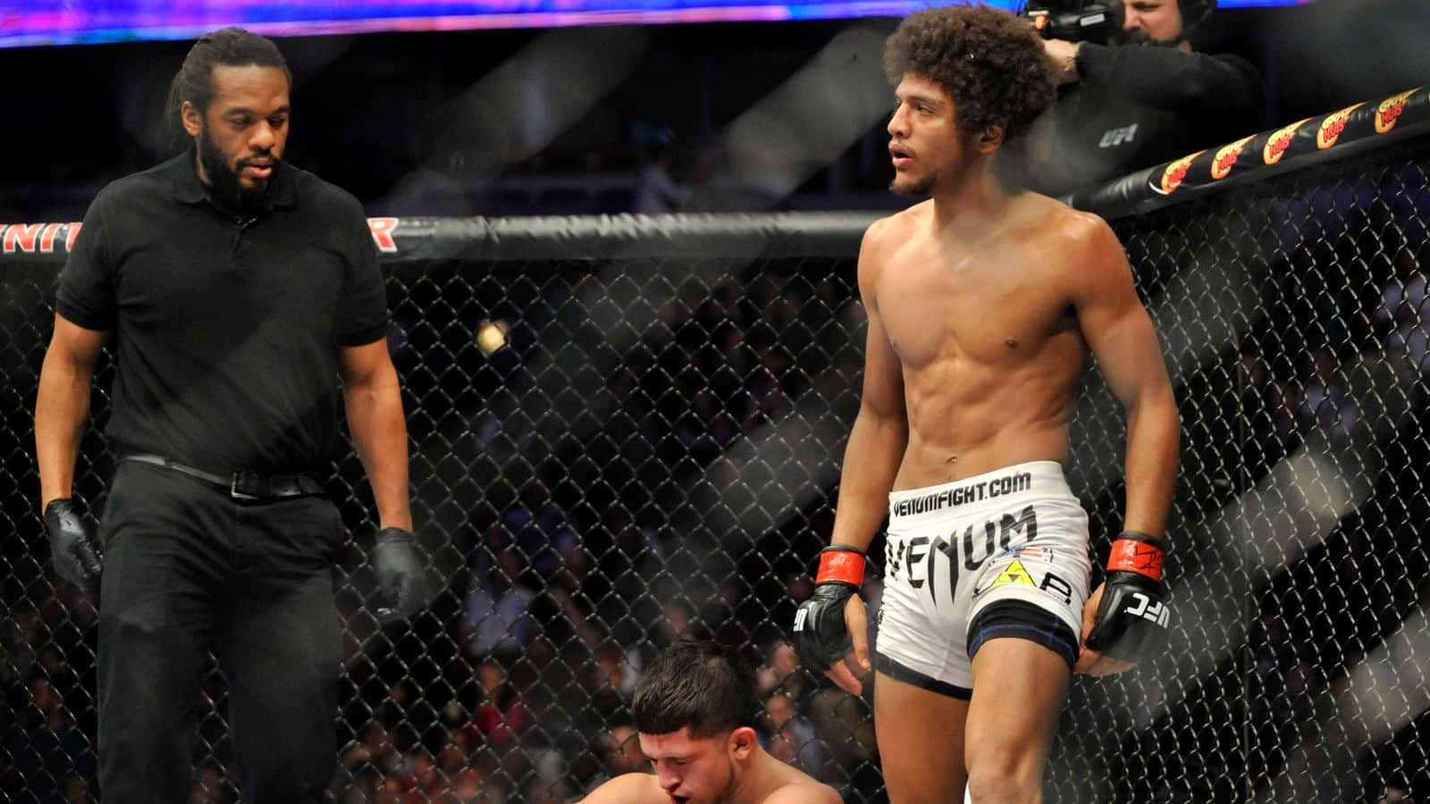 MMA戰士在八角籠中站在被擊敗的對手上方，裁判在附近。