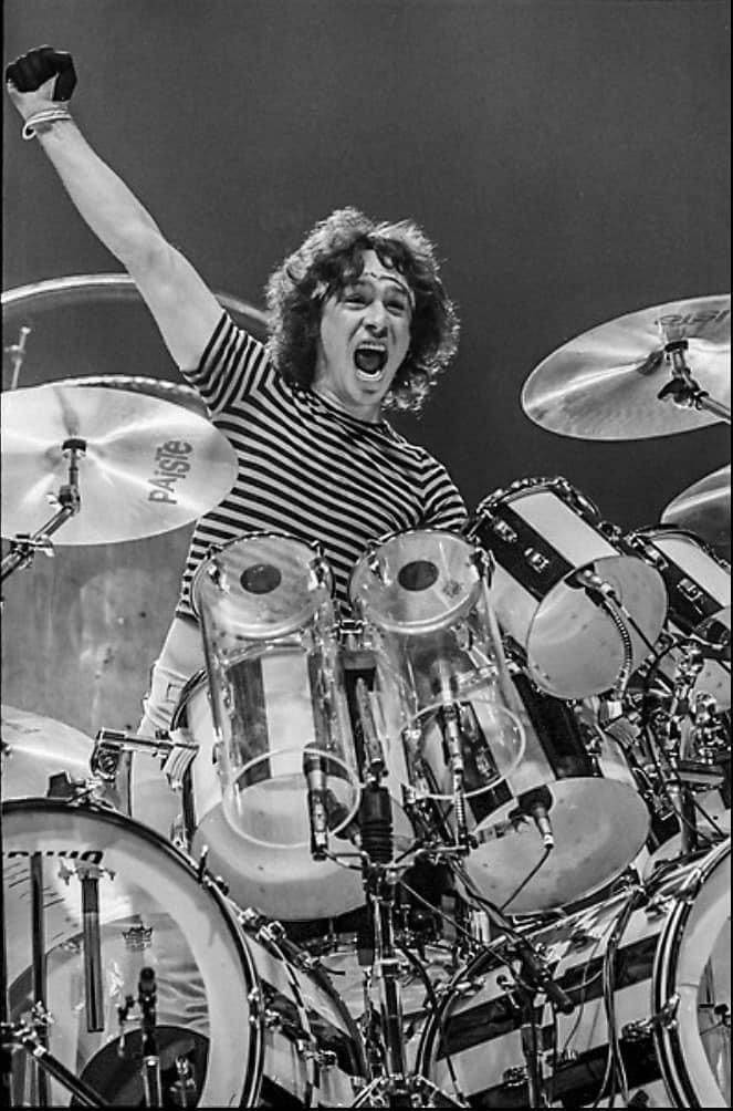 Alex Van Halen 樂隊演奏 壁紙 — 一張黑白照片，拍攝鼓手在表演中，在複雜的鼓組後方高舉一隻手臂，展現勝利姿態。