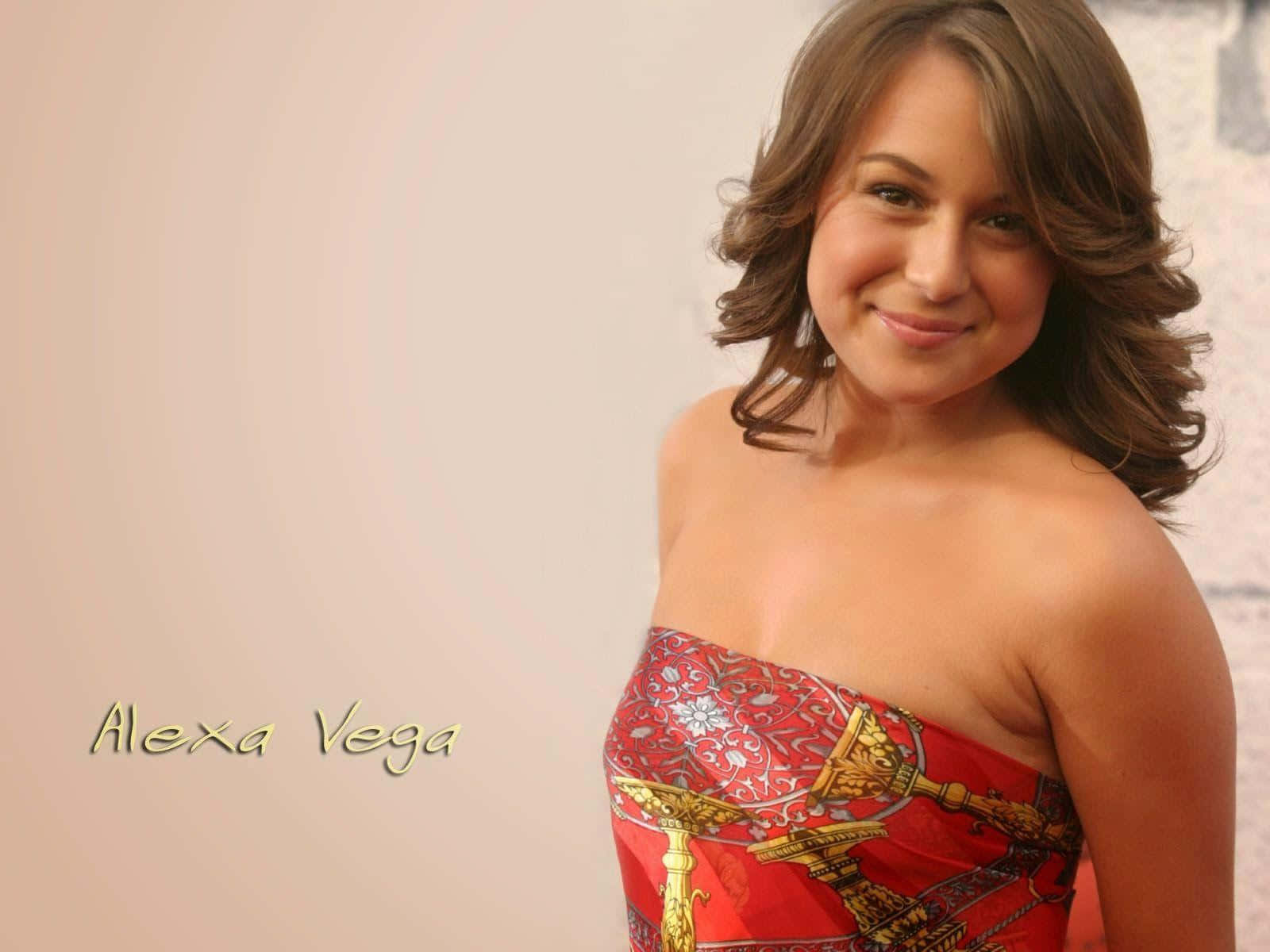 Alexa Penavega 桌布 壁紙 — Alexa Vega 喺柔和米色背景前，穿著鮮豔紅色圖案嘅露肩連身裙，溫暖咁微笑。