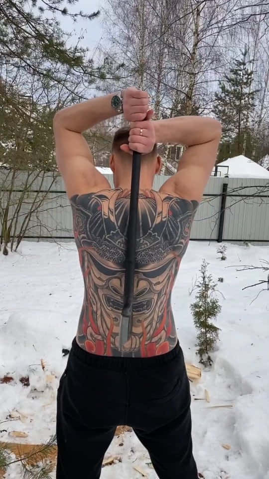 一個有紋身的男人在雪地冬季戶外將桿子舉過頭頂。