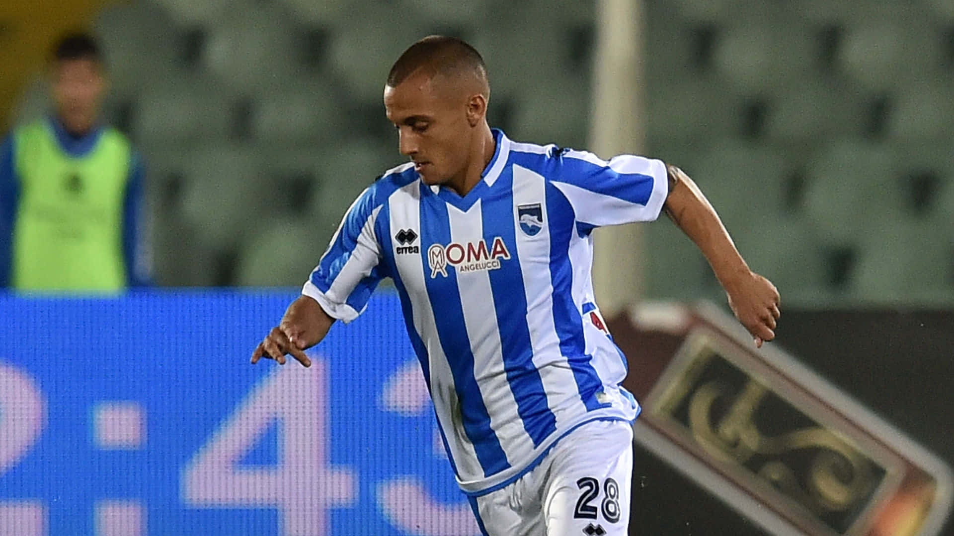 Alexandru Mitrita 對陣 FC Torino 壁紙 — 一名身穿藍白間條球衣的足球運動員在明亮的燈光下於球場上動態奔跑。