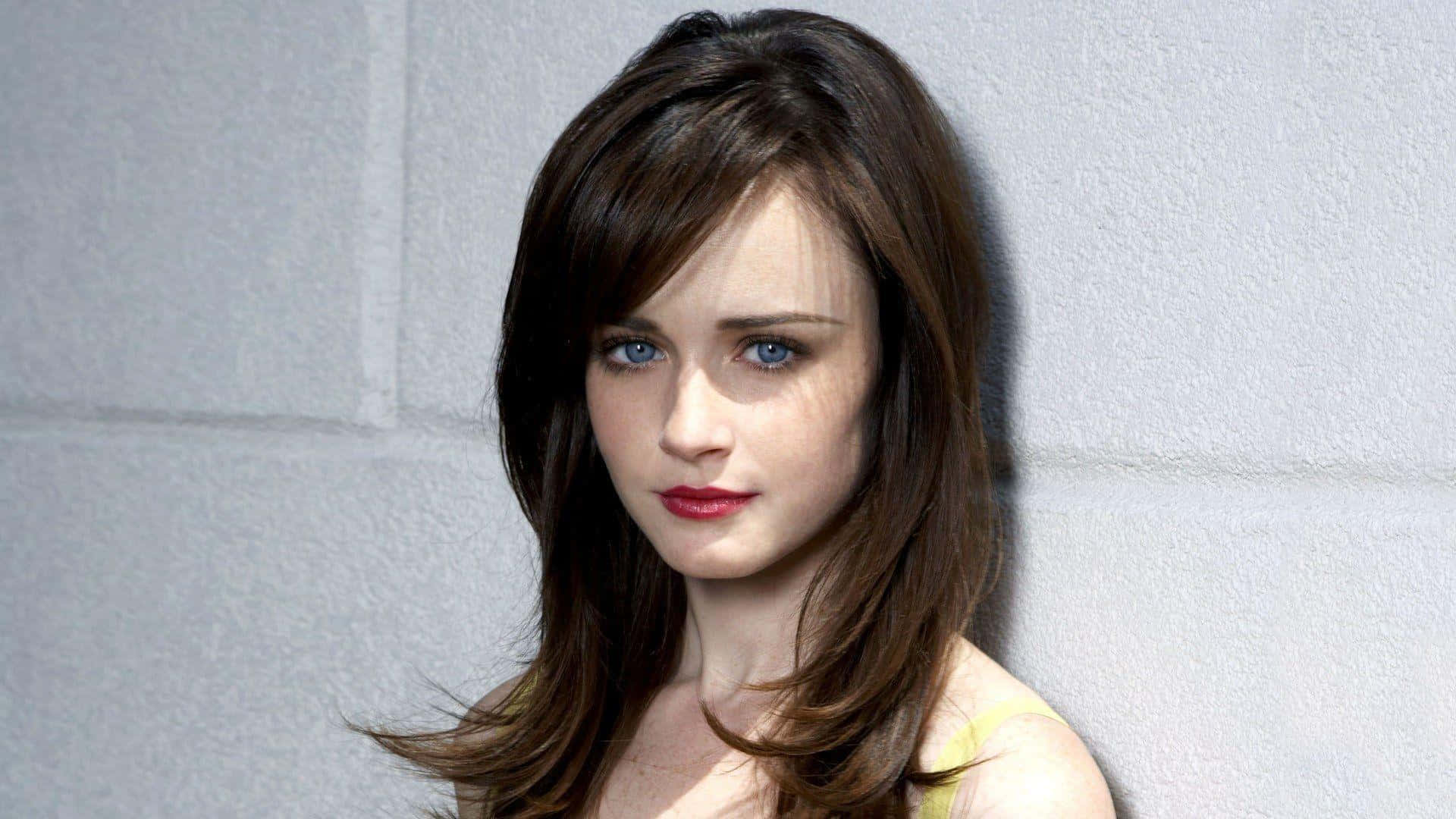 Alexis Bledel 精緻寫真拍攝 壁紙 — 一位擁有引人注目的藍色眼睛和棕色頭髮的女性靠著紋理灰色牆壁，穿著黃色上衣和紅色唇膏。