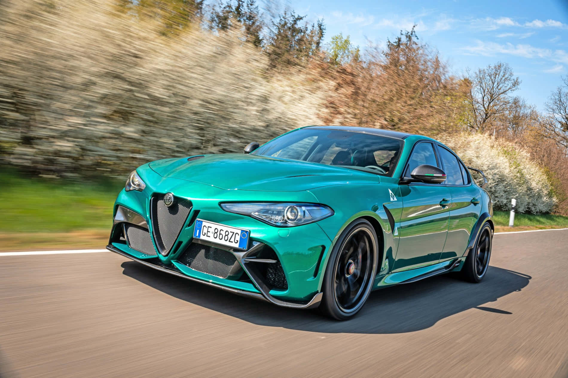 邁向未來，駕馭經典Alfa Romeo 壁紙 — 一輛充滿活力的綠色愛快羅密歐Giulia Quadrifoglio在陽光明媚的道路上疾馳，模糊的秋葉飛掠而過。