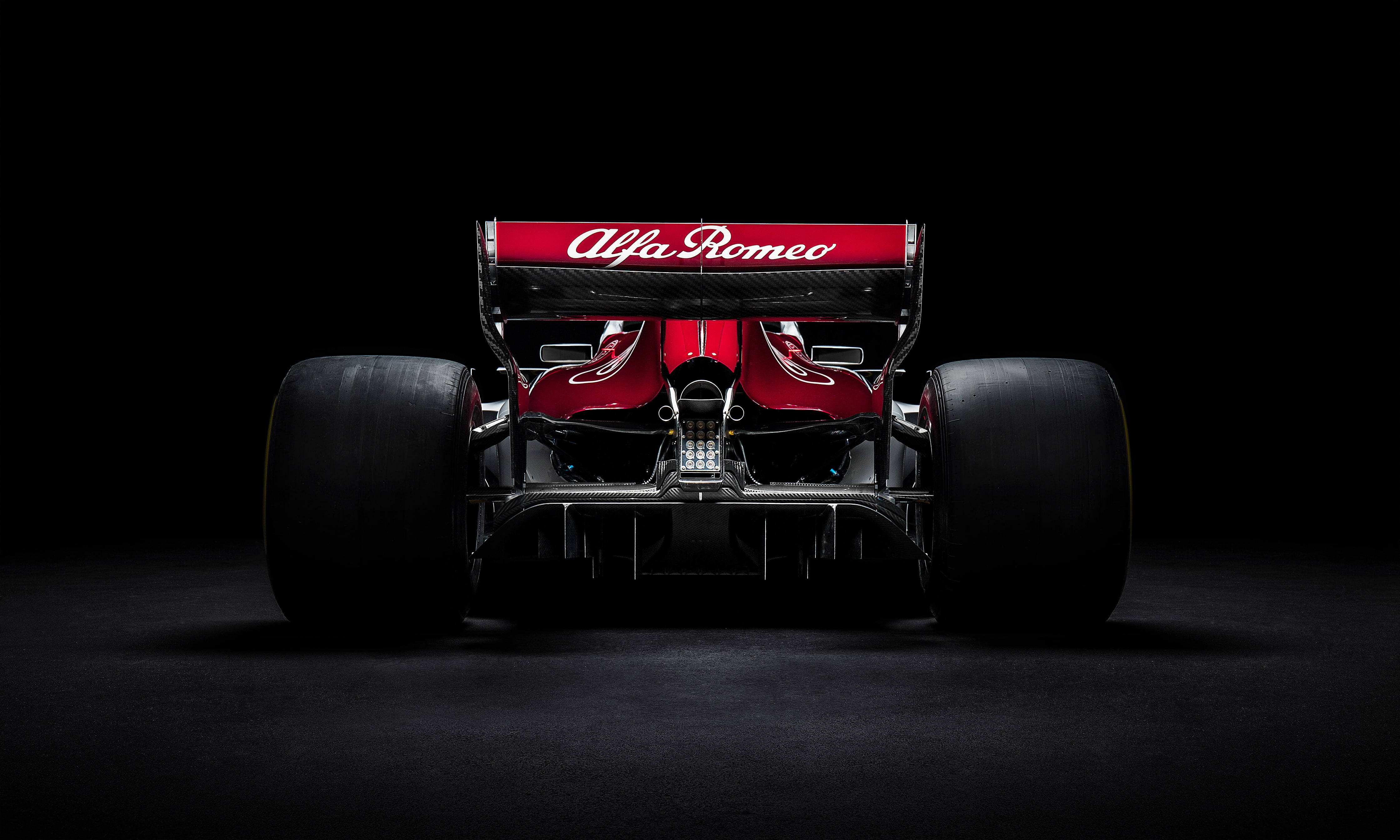 Alfa-Romeo F1 Sauber 2018 壁紙 — 一輛流線型的紅色愛快羅密歐一級方程式賽車，在漆黑的攝影棚背景下，從下方被戲劇性地照亮。