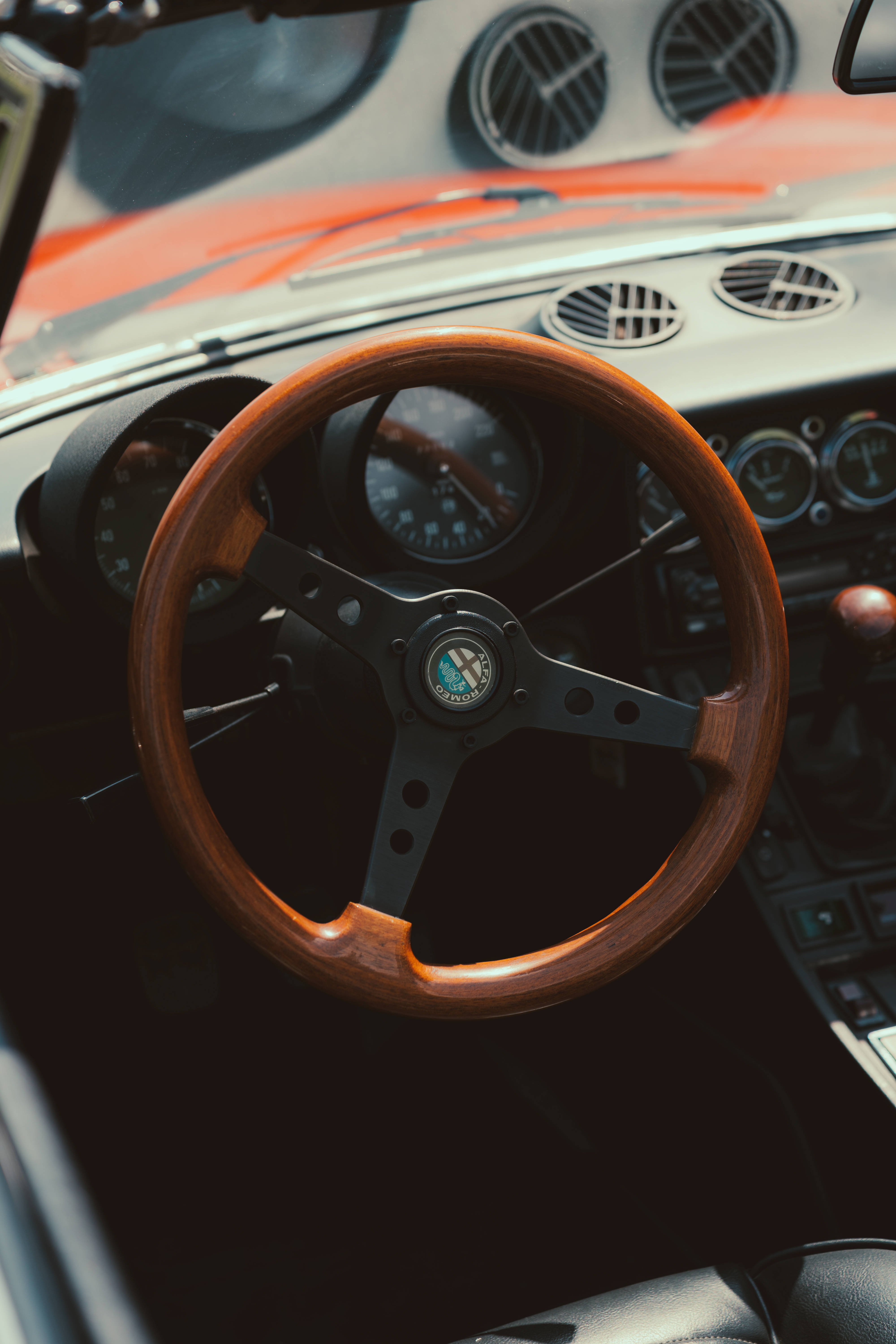 Alfa Romeo iPhone 方向盤 壁紙 — 暖陽下，復古愛快羅密歐跑車內飾特寫，配備木質方向盤和模擬儀錶。