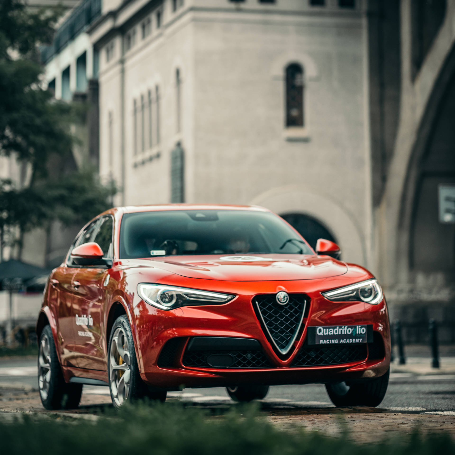 紅色愛快羅密歐 Quadrifoglio 賽車停泊在歷史建築附近的鵝卵石街道上。