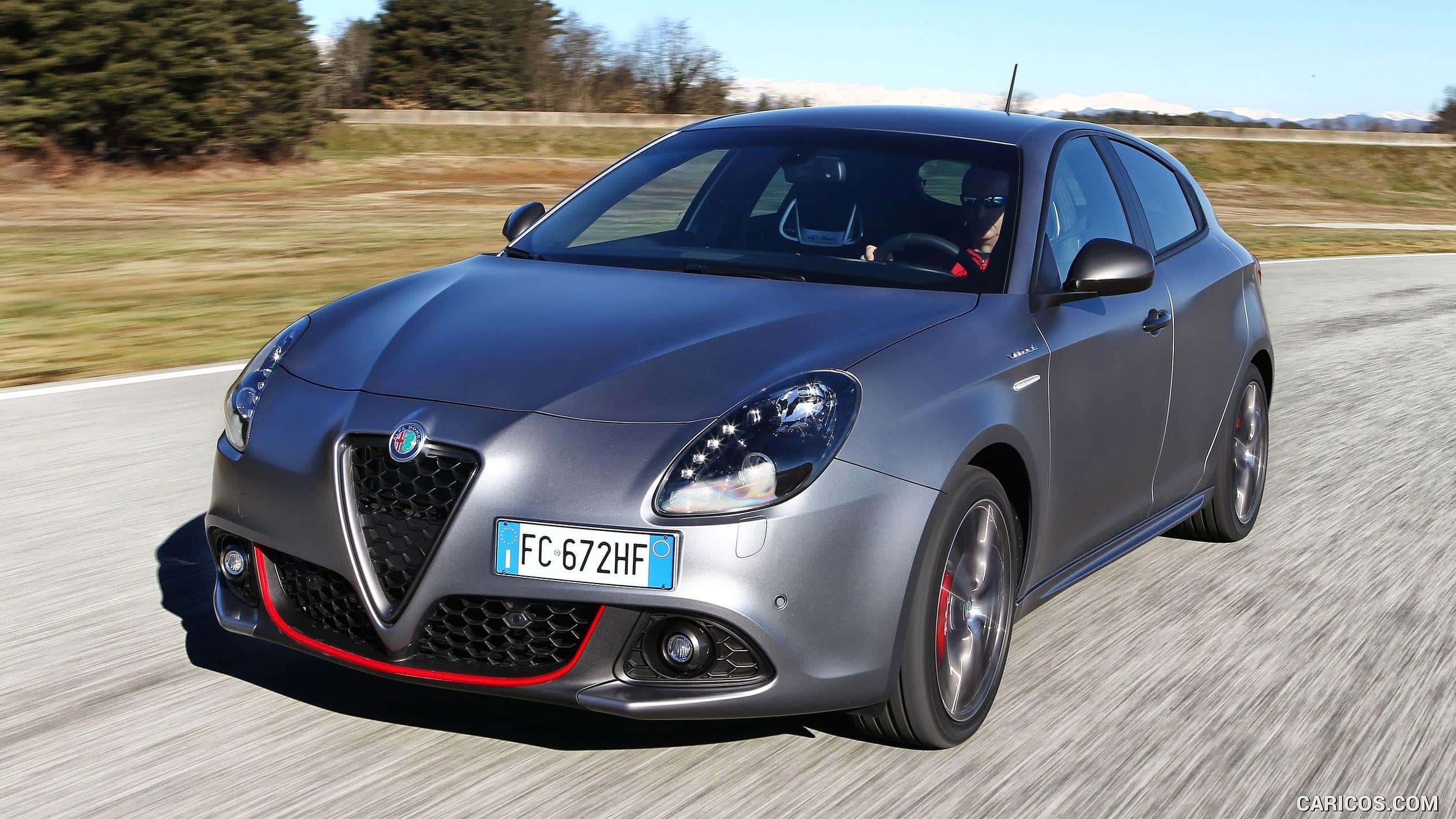 Alfa Romeo——義大利卓越的象徵 壁紙 — 一輛流線型的銀色愛快羅密歐Giulietta在陽光明媚的鄉村道路上疾馳，帶有模糊的動感和紅色點綴。