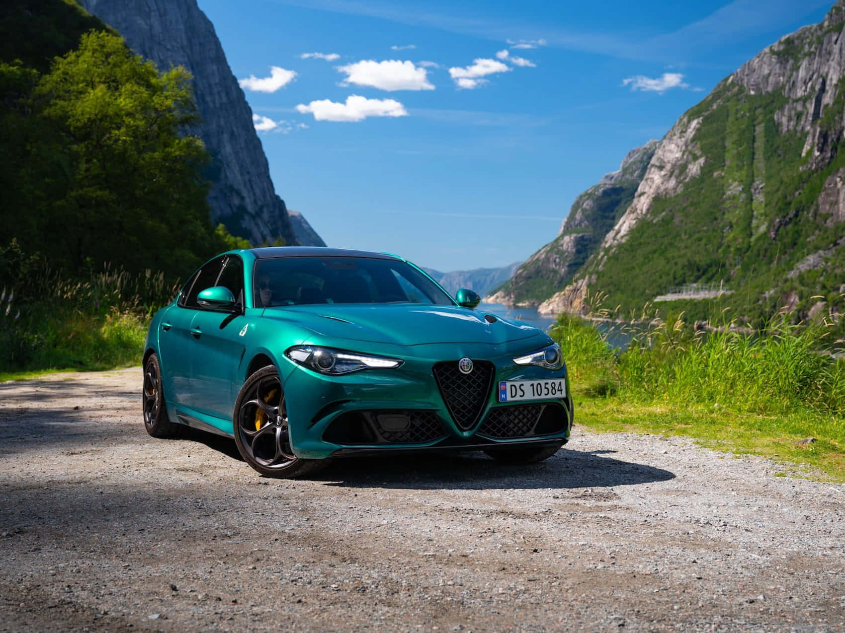 青綠色Alfa Romeo房車泊喺碎石路旁邊峽灣山脈