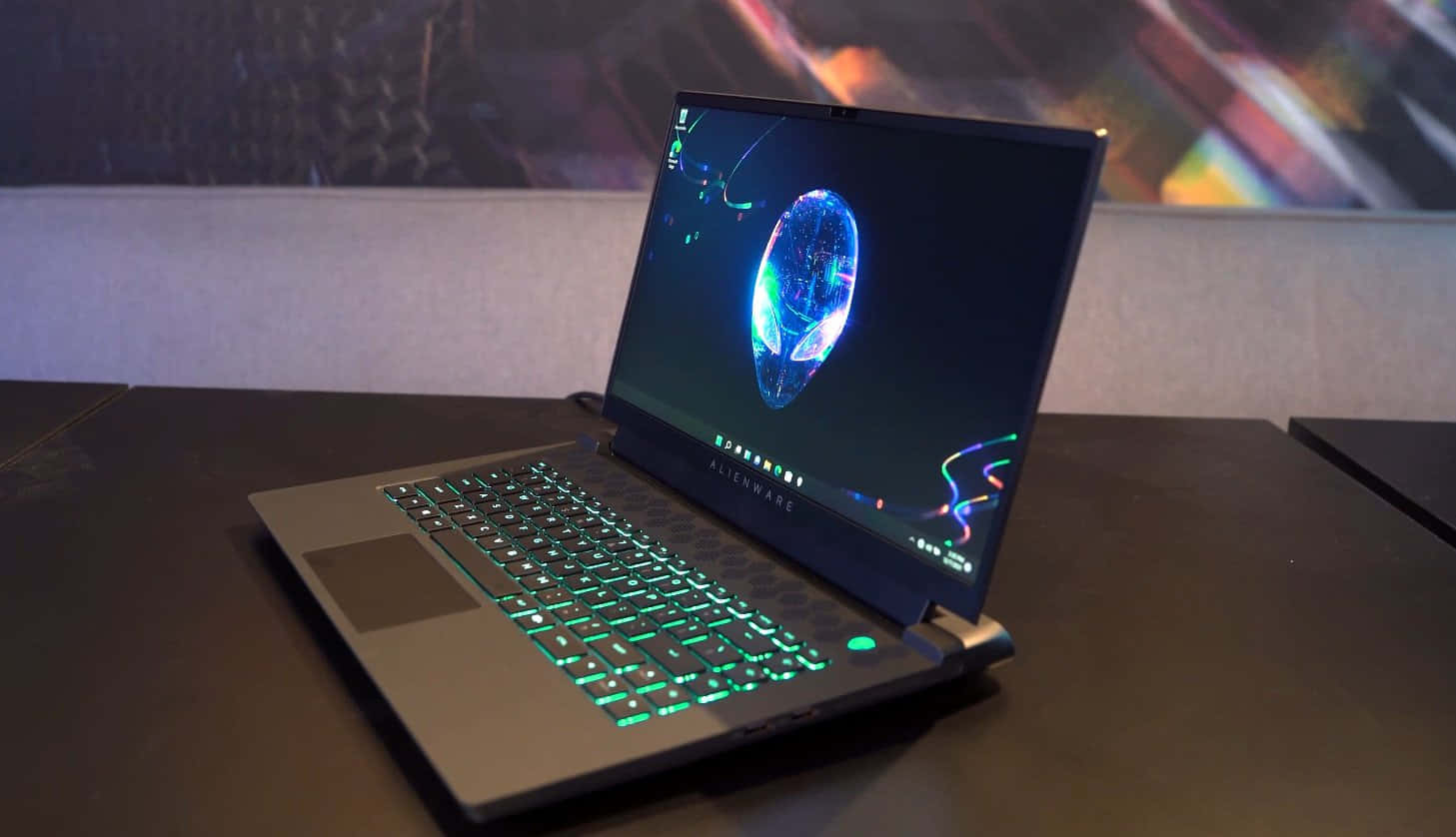以 Alienware 照亮未來 壁紙 — Alienware 手提電腦配備發光綠色鍵盤，在黑暗的桌子上打開，屏幕上顯示一個充滿活力的藍色全息球體。