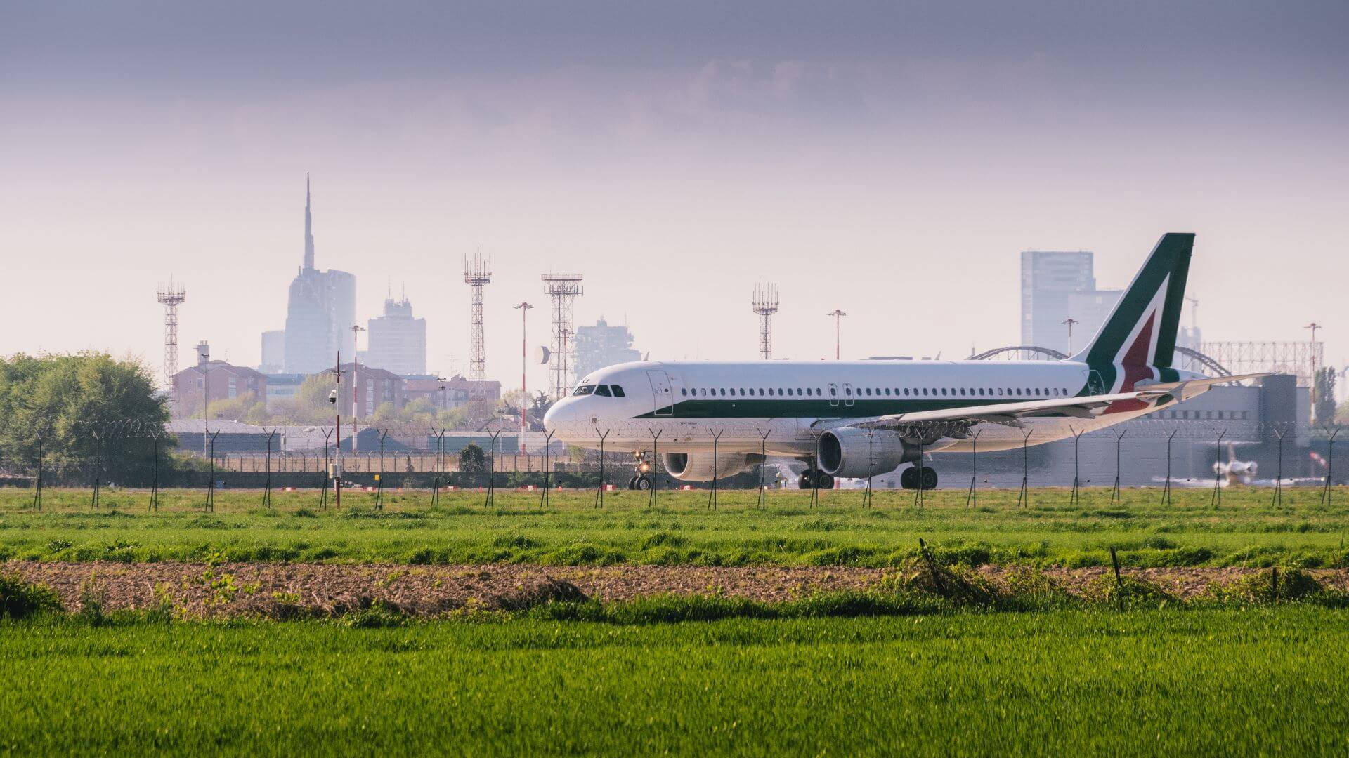 意大利航空飛機在跑道上，背景有綠色田野和城市天際線