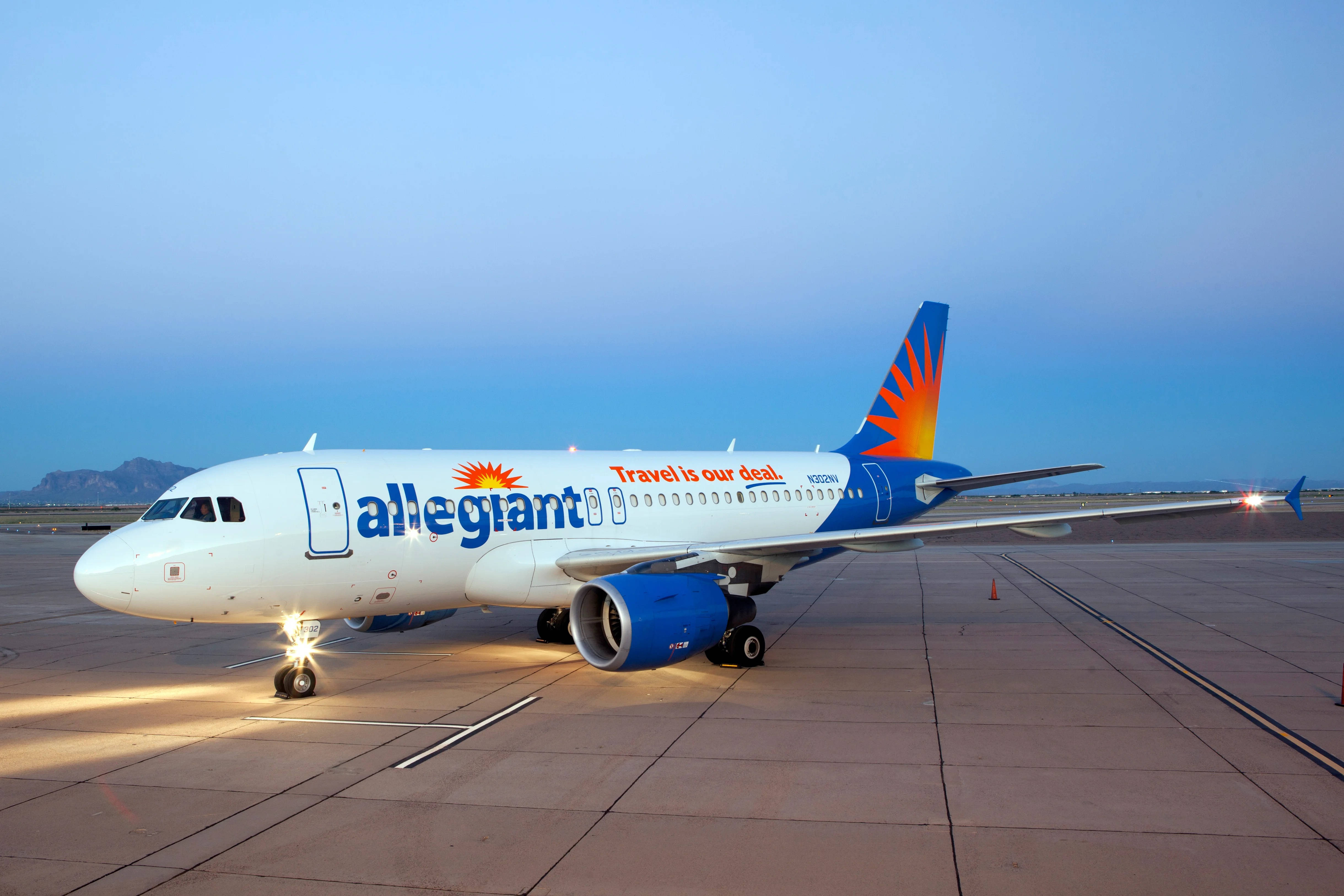 Allegiant Air 飛機停泊跑道 壁紙 — 一架忠實航空客機在黃昏時停在機場停機坪上，溫暖的地面燈光照亮其白色和藍色機身，映襯著漸暗的天空。