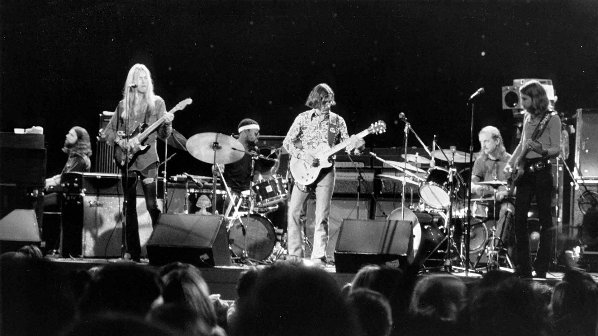 Allman Brothers Band 演唱會黑白照片 壁紙 — 一張黑白照片，搖滾樂隊在明亮的舞台燈光下，用結他、鼓和擴音器現場表演。