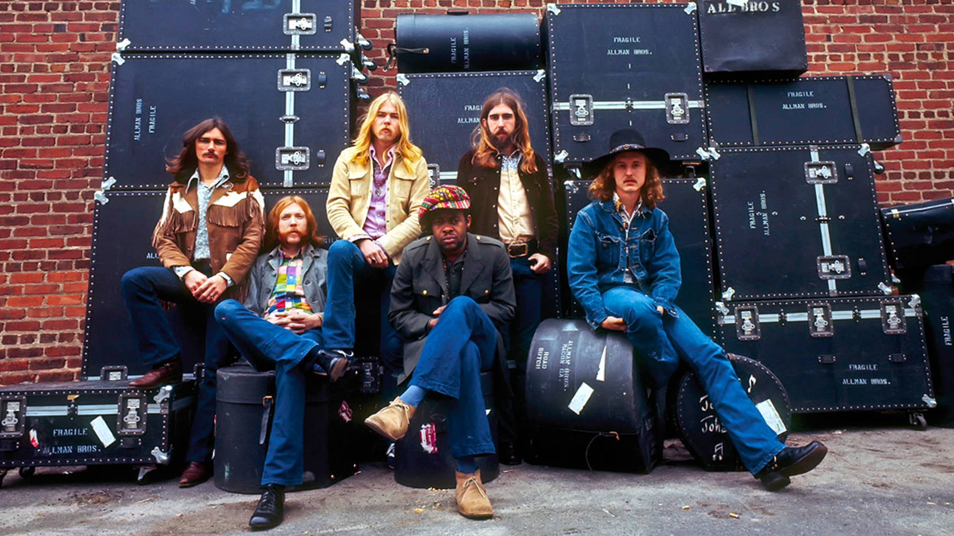Allman Brothers Band 成員 壁紙 — Allman Brothers Band 的六位成員隨意地靠在磚牆上，周圍環繞著他們的黑色設備箱。