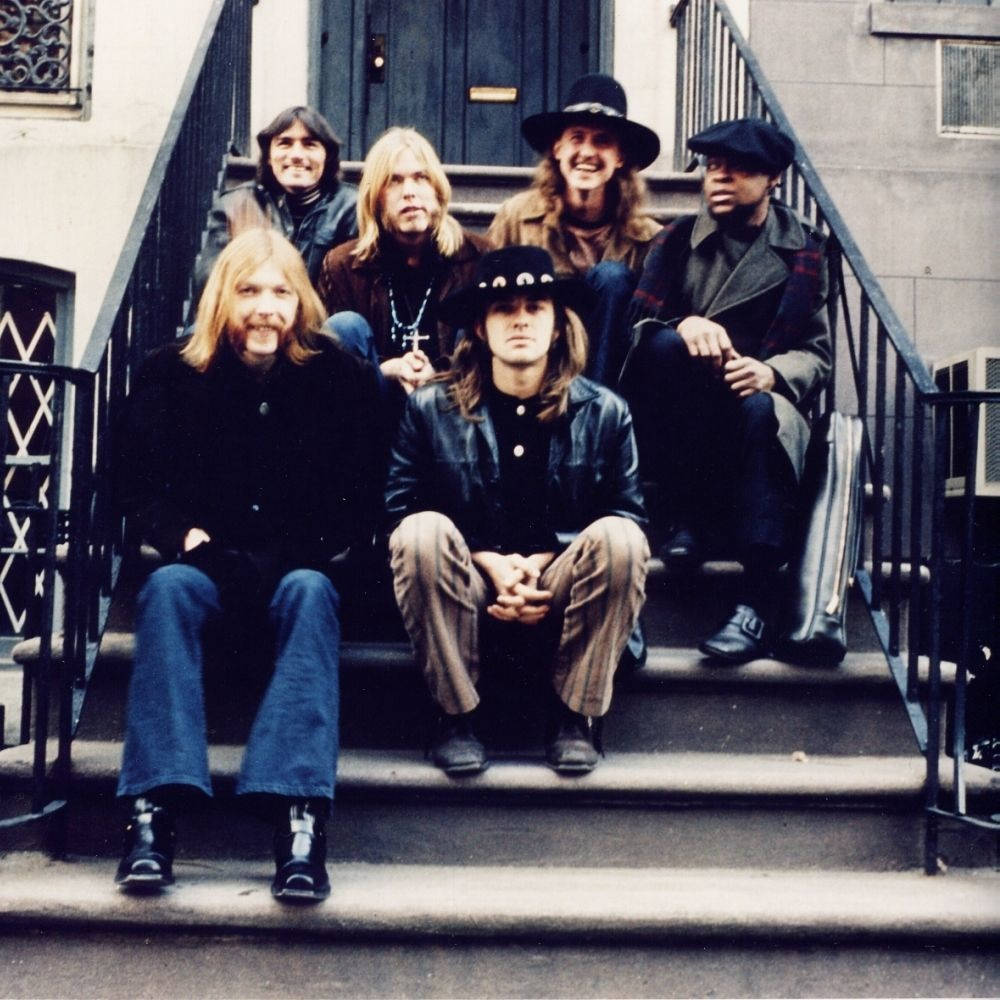 Allman Brothers Band《One Way Out》演出現場 壁紙 — 七位長髮戴帽子的男士穿著復古皮褸和牛仔褲，在戶外混凝土樓梯上擺姿勢。