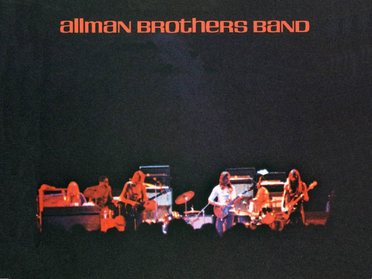Allman Brothers Band 演唱會現場 壁紙 — 一張奧曼兄弟樂隊的現場音樂會照片，在黑暗背景下沐浴在溫暖的橙色舞台燈光中。