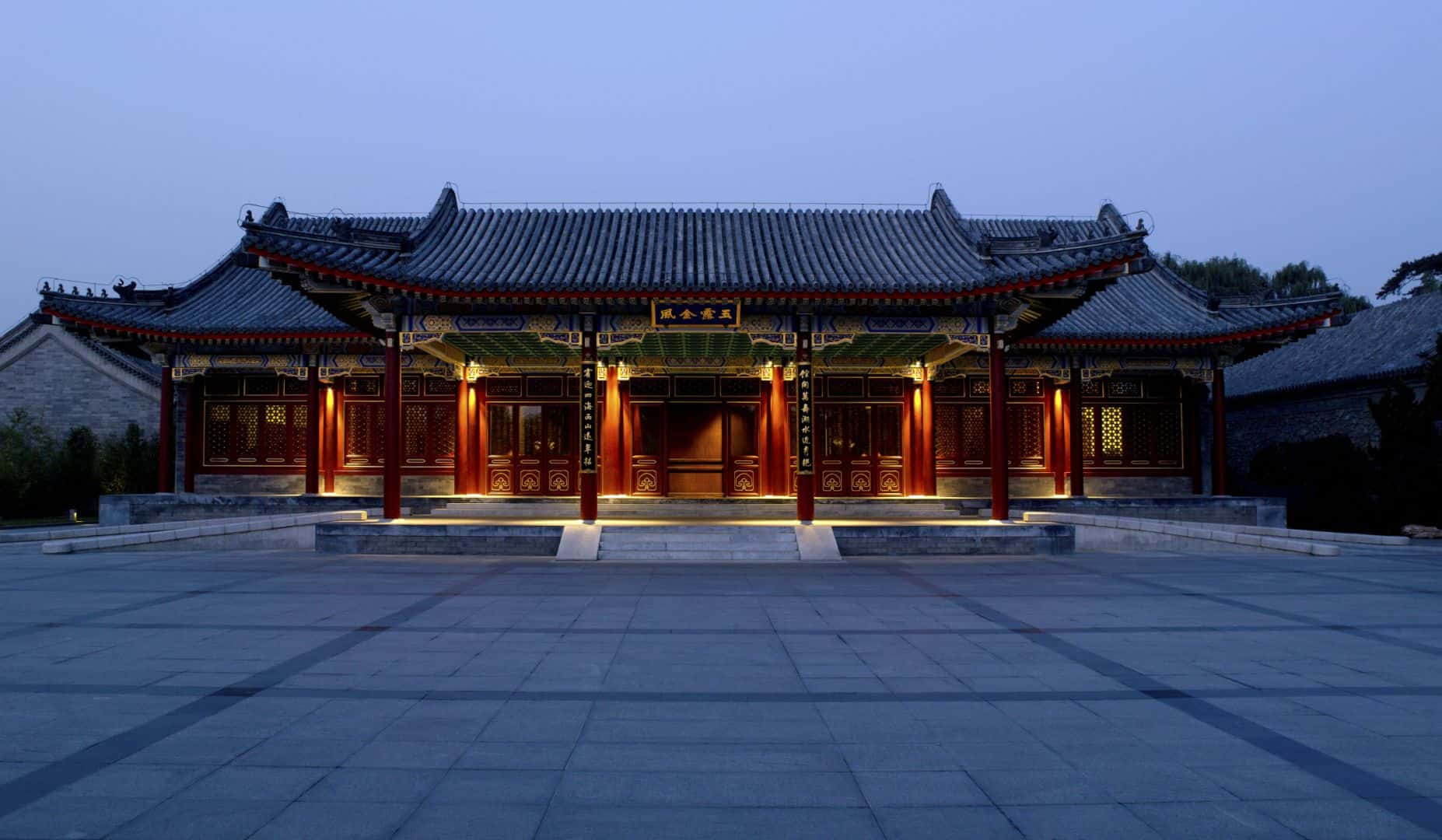 Aman圓明園正面視角 壁紙 — 一座宏偉的傳統中式亭閣，紅色柱子和瓦片屋頂在暮色天空下溫暖地發光。