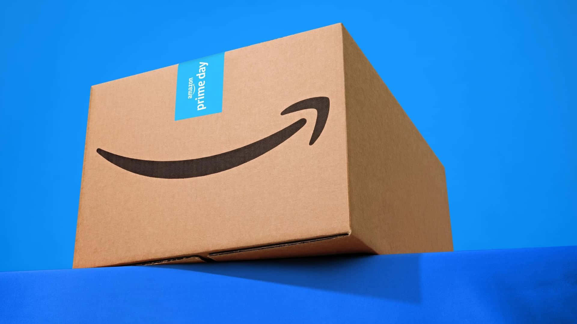  壁紙 — 一個帶有藍色標籤的棕色Amazon Prime Day紙箱放在鮮豔的藍色表面上，背景為純藍色。