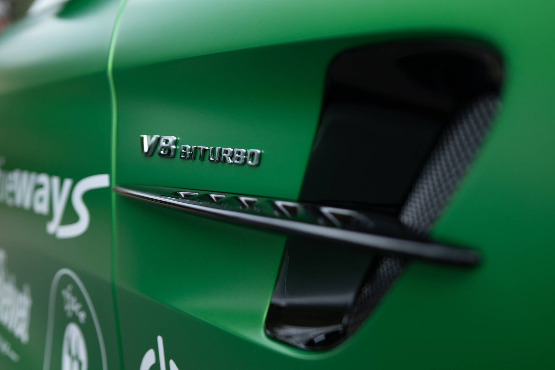 綠色跑車車門特寫，帶有 V8 BITURBO 徽章和碳纖維通風口。