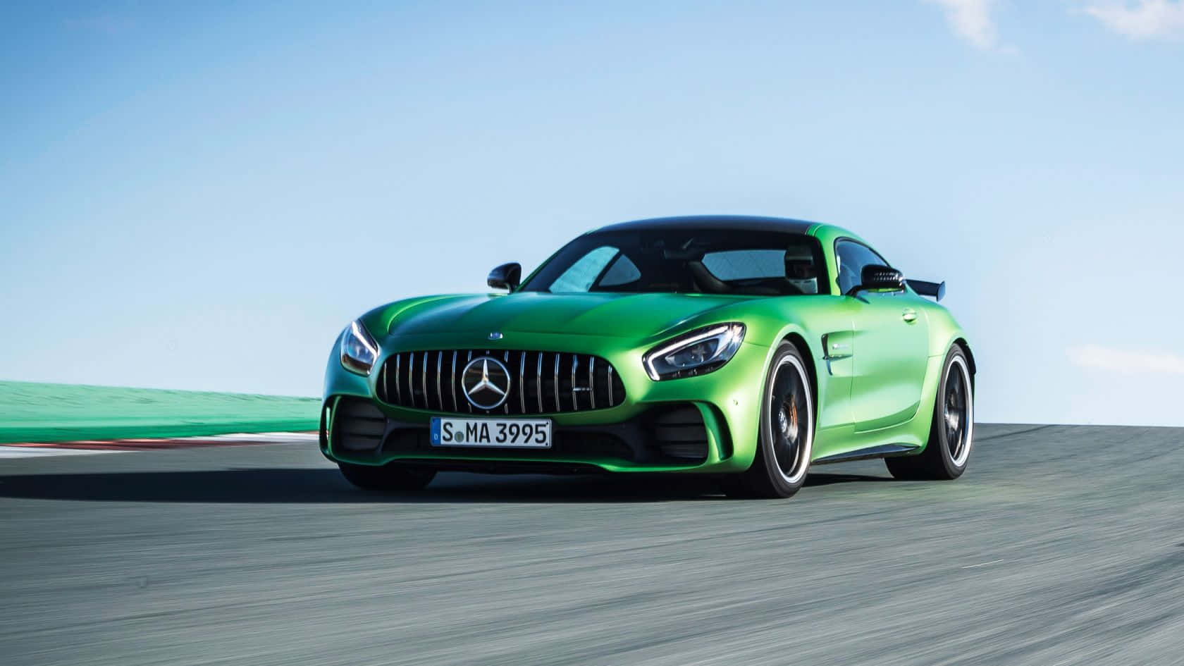 時尚的AMG GT-R — 現代最出色的性能車之一 壁紙 — 一輛充滿活力的綠色 Mercedes-AMG GT R 跑車在晴朗的藍天下沿著賽道飛馳。