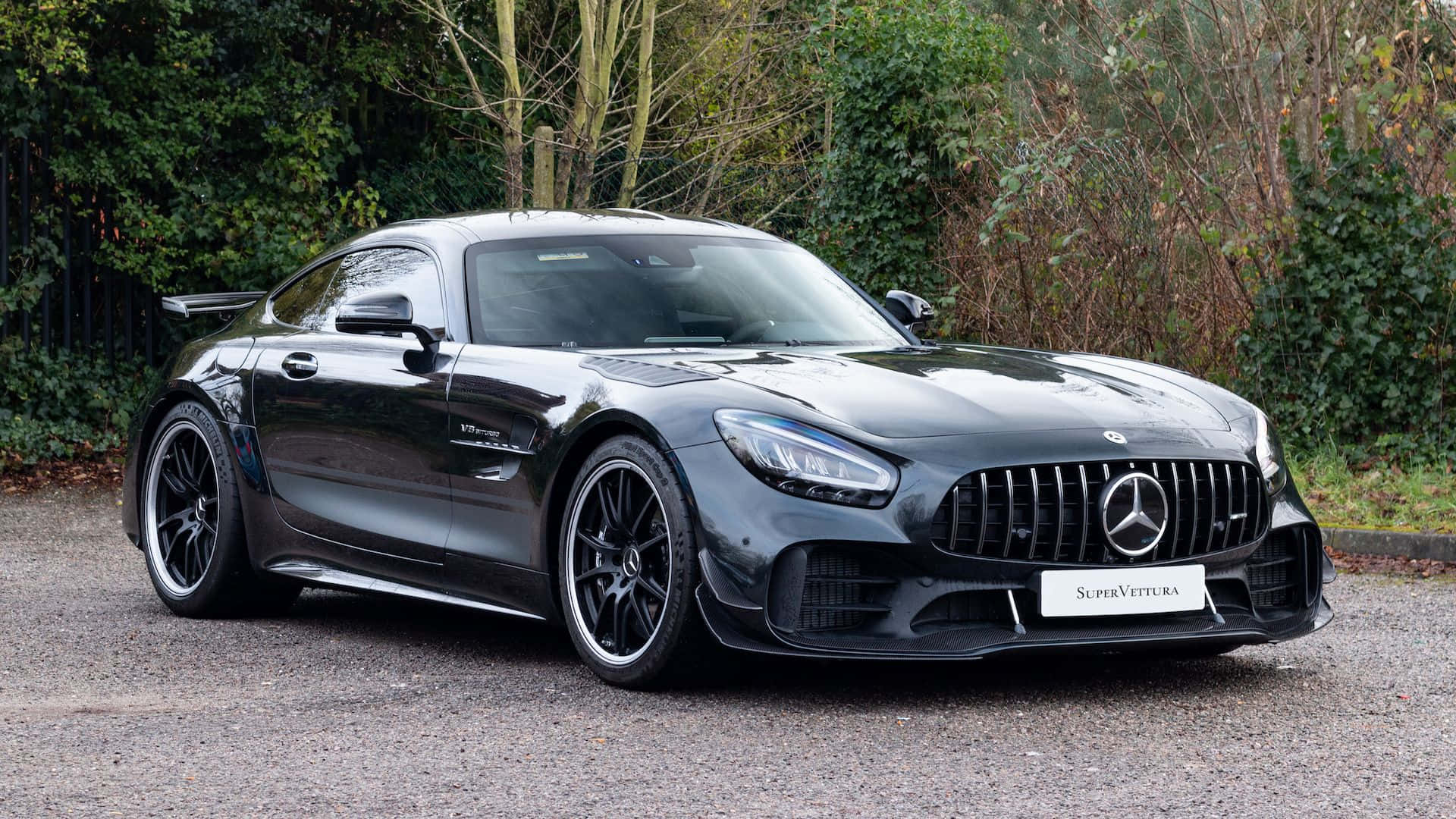 震撼的梅賽德斯AMG GT-R對比強烈背景 壁紙 — 一架時尚的黑色Mercedes-AMG GT Black Series超級跑車停在碎石上，背景有綠色的灌木叢。