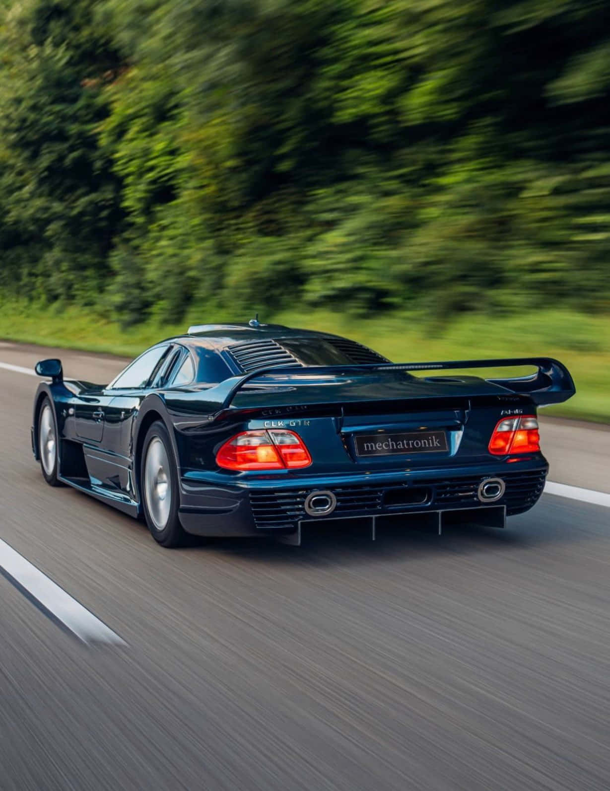藍色AMG GT-R綠樹安卓背景 壁紙 — 一架時尚的深藍色 Mercedes CLK GTR 在樹林環繞的道路上疾馳，動態模糊效果突顯其力量與速度。