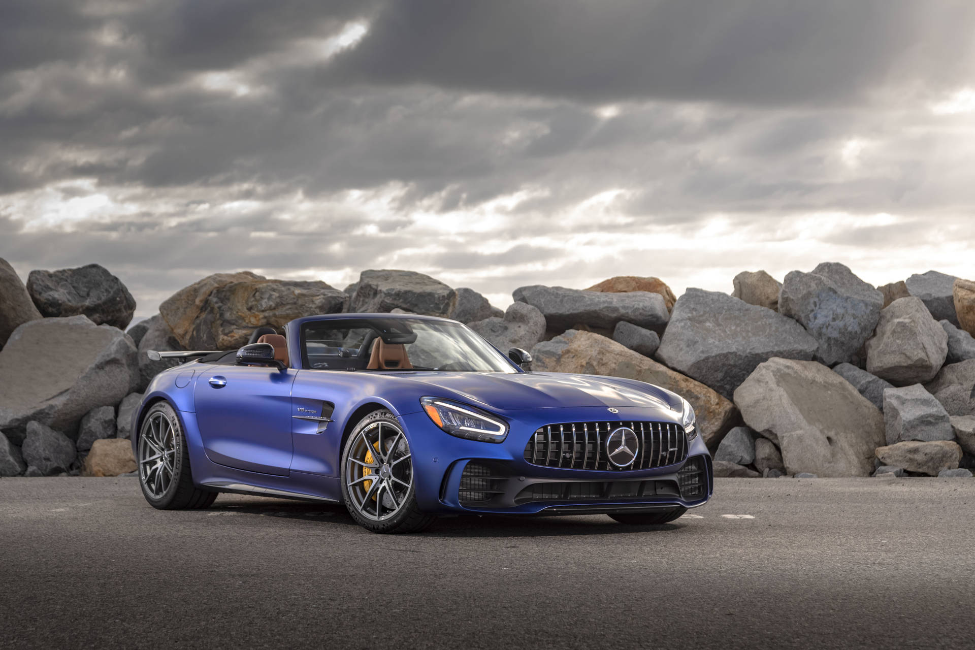 藍色 Mercedes-AMG GT R 開篷車停泊在岩石附近，天空多雲。