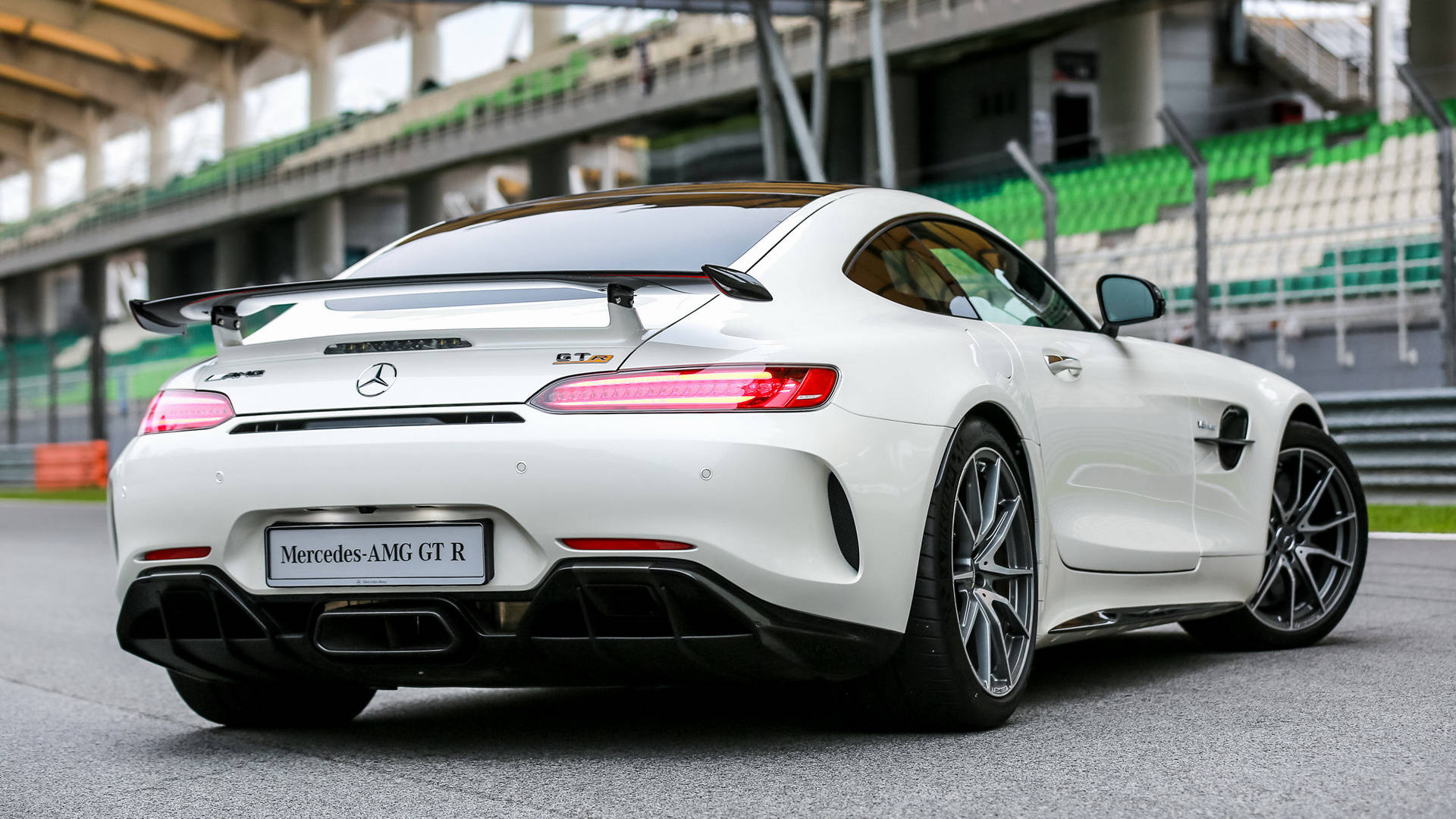 白色 Mercedes-AMG GT R 跑車在賽車場上，背景有看台。
